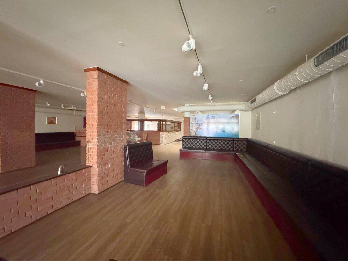 Großer Raum mit Holzboden, gemauerten Säulen und Sitzbänken.