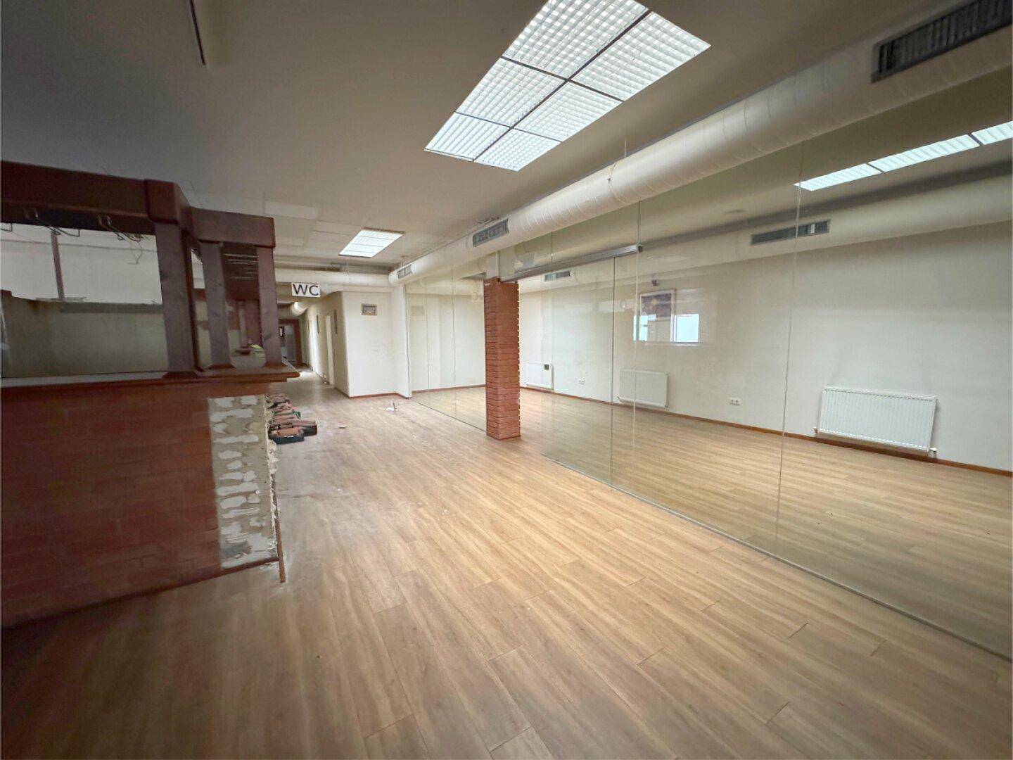 Heller, offener Raum mit Holzboden, Spiegelwänden und Heizkörpern.