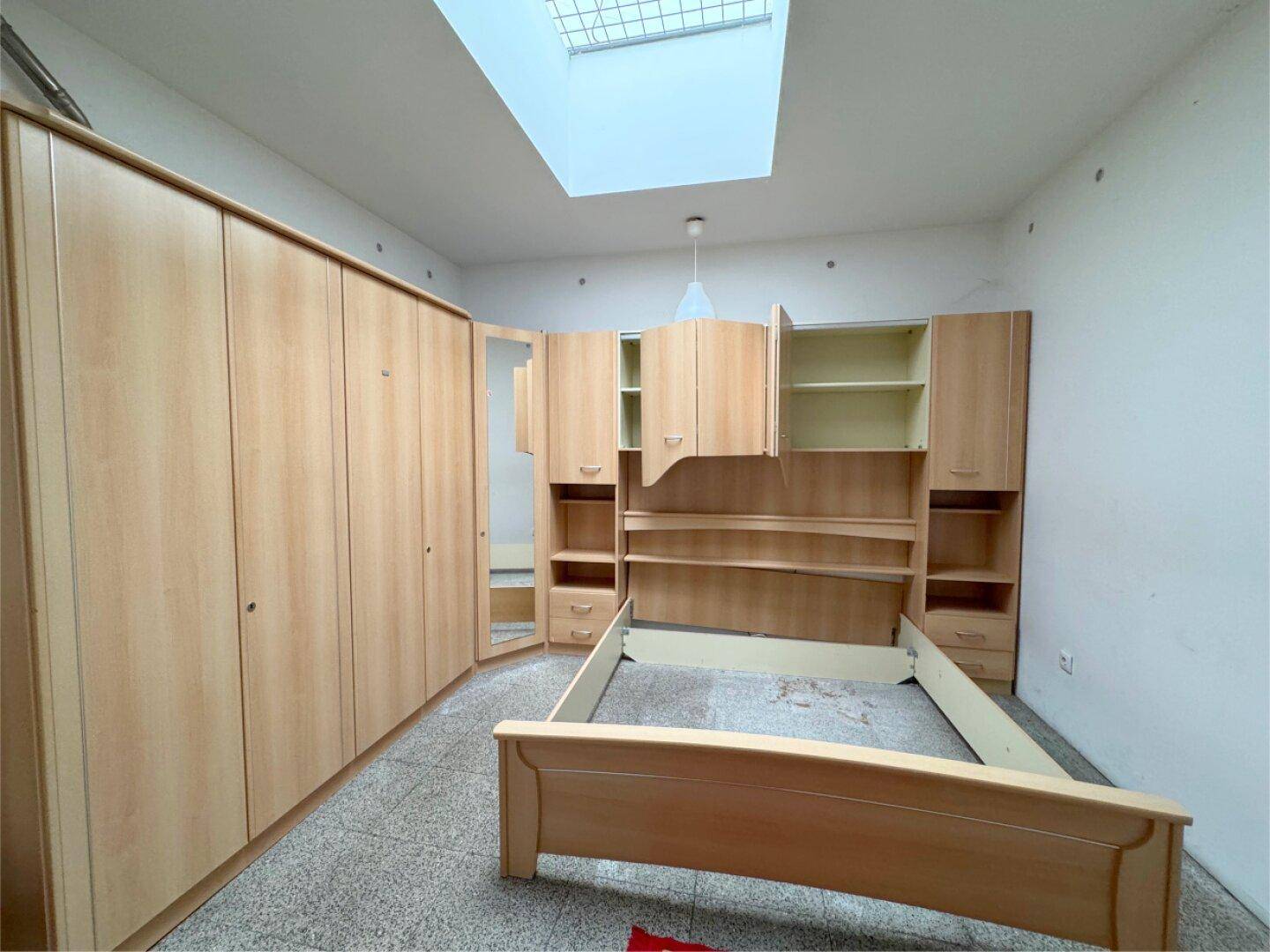 Schlafzimmer mit Einbauschränken, Bettrahmen und Oberlicht für natürliches Licht.