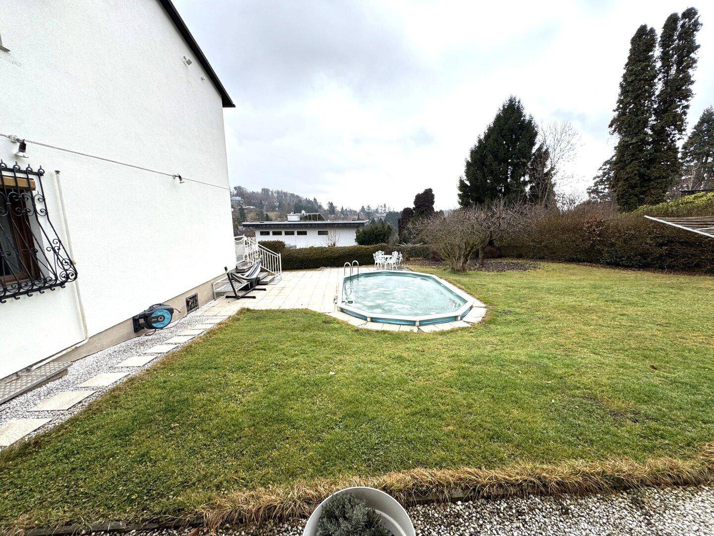 Gartenbereich mit einem ovalen Pool, einer gepflasterten Terrasse und Rasenfläche.