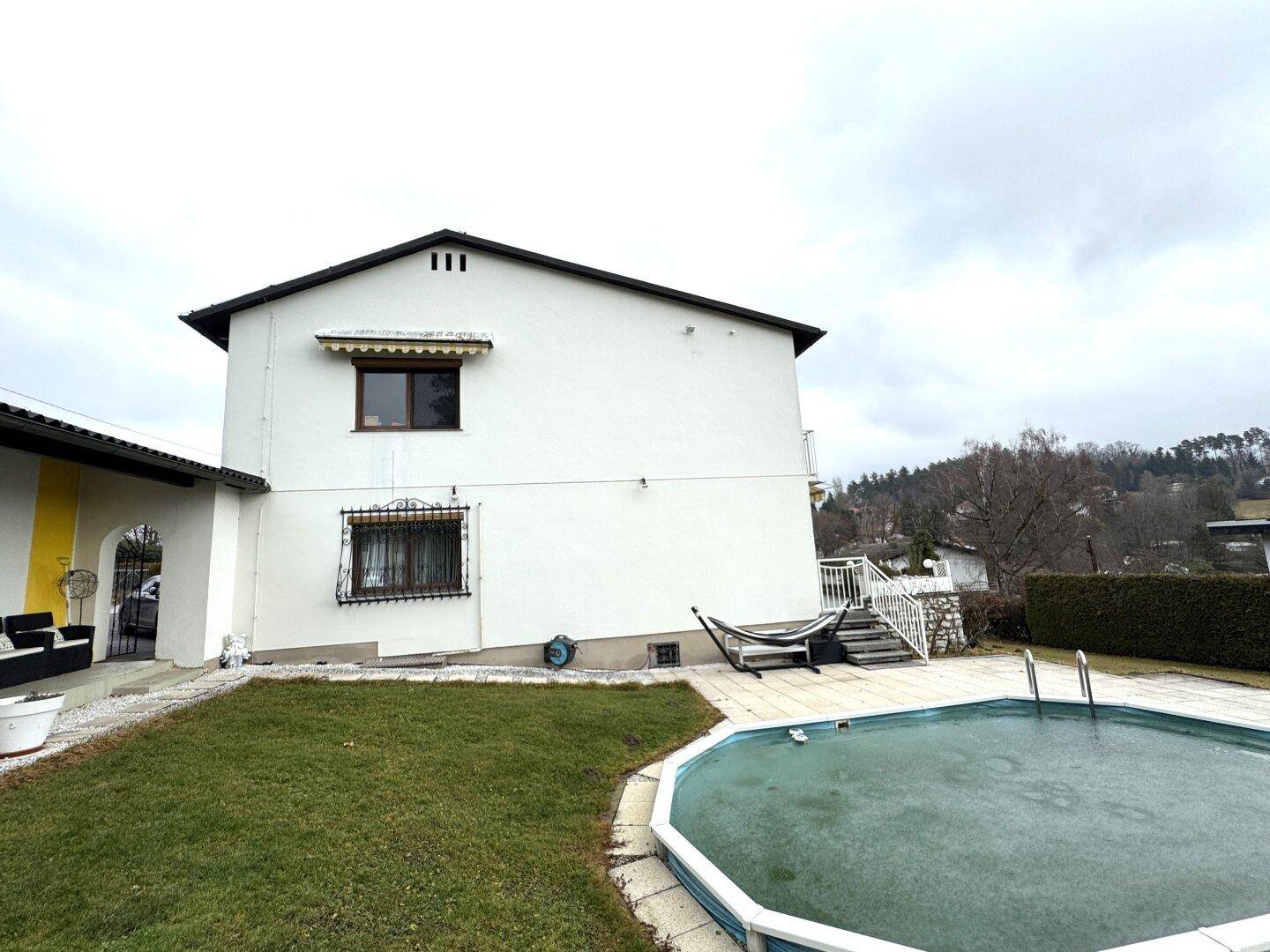 Hausfassade von der Seite mit Pool, Rasen und umliegender Grünfläche.