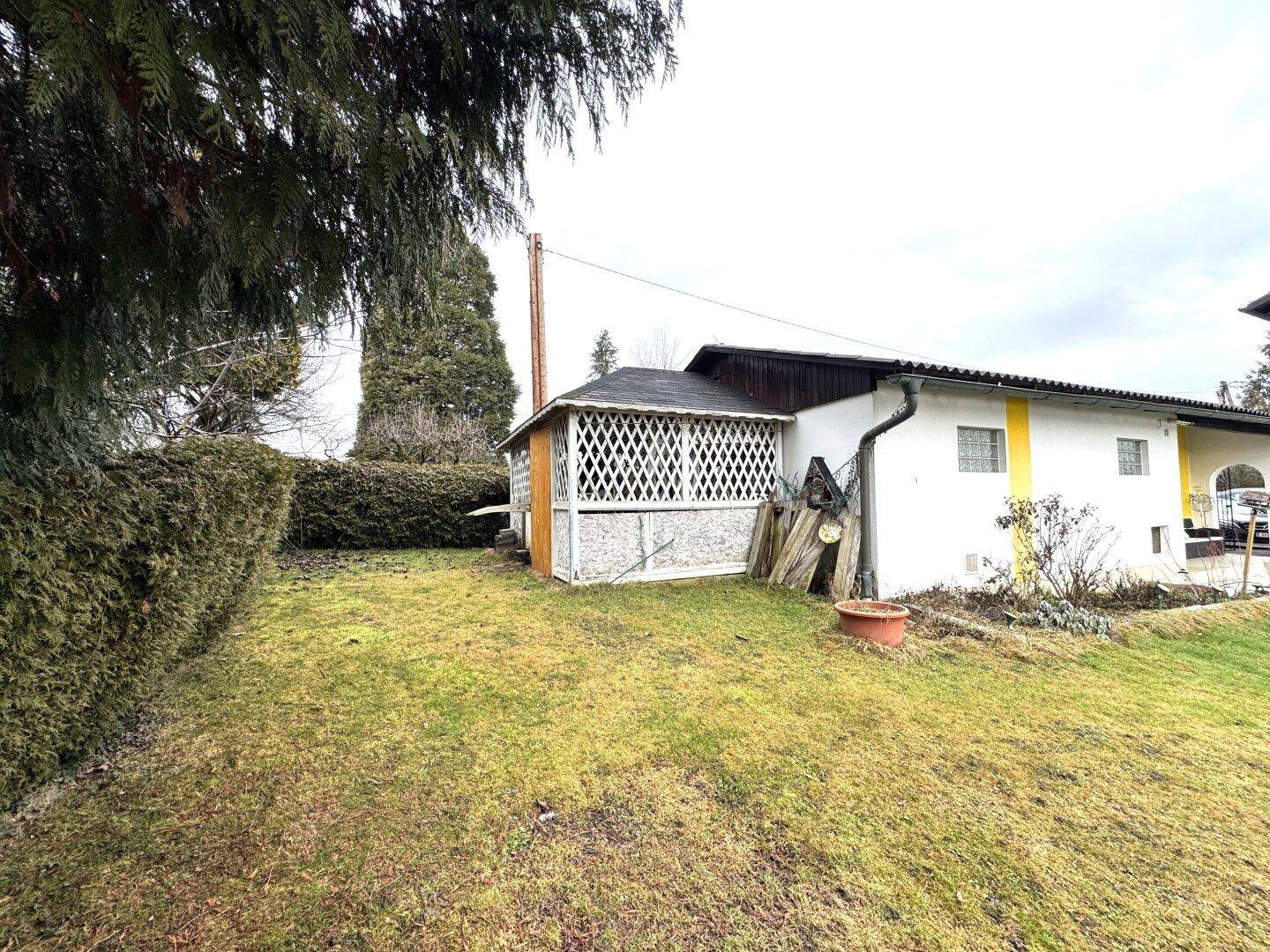 Gartenbereich mit einem kleinen Holzschuppen, Hecke und Rasenfläche.