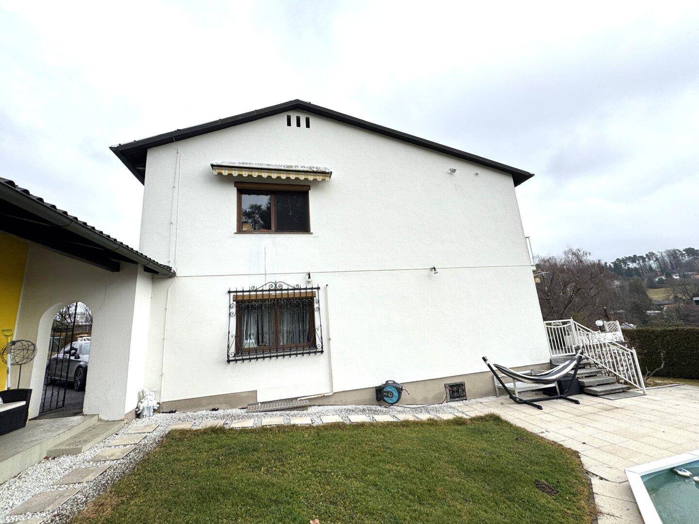 Seitenansicht des Hauses mit Poolbereich und gepflegtem Rasen unter bewölktem Himmel.