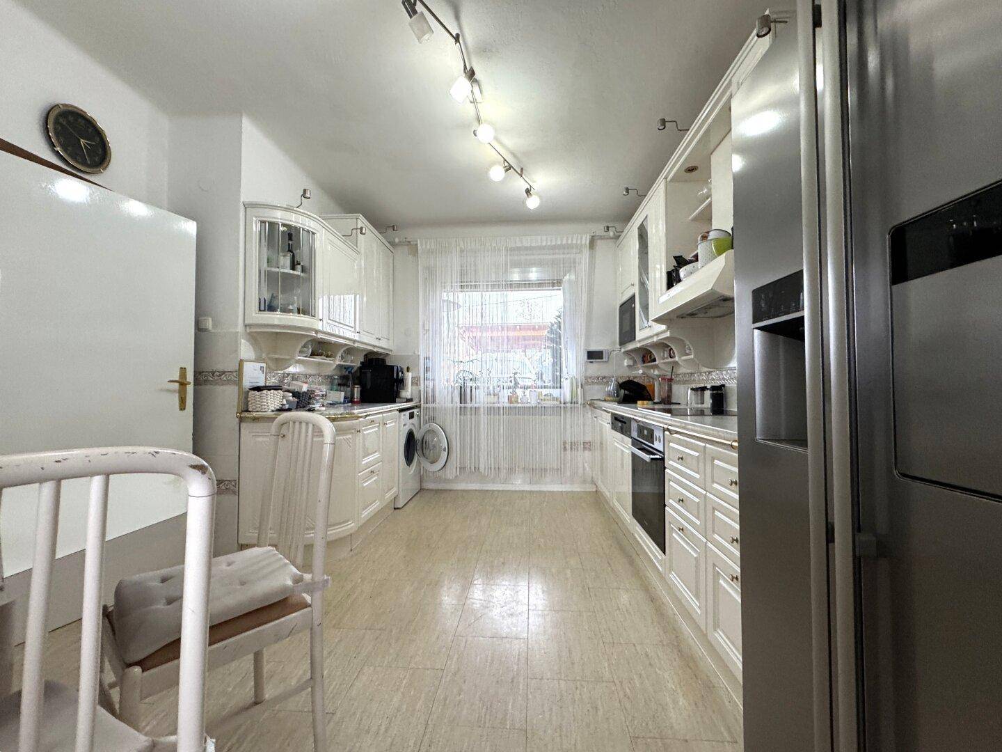 Funktionale Küche mit weißen Einbauschränken, Geräten und einem Fenster.