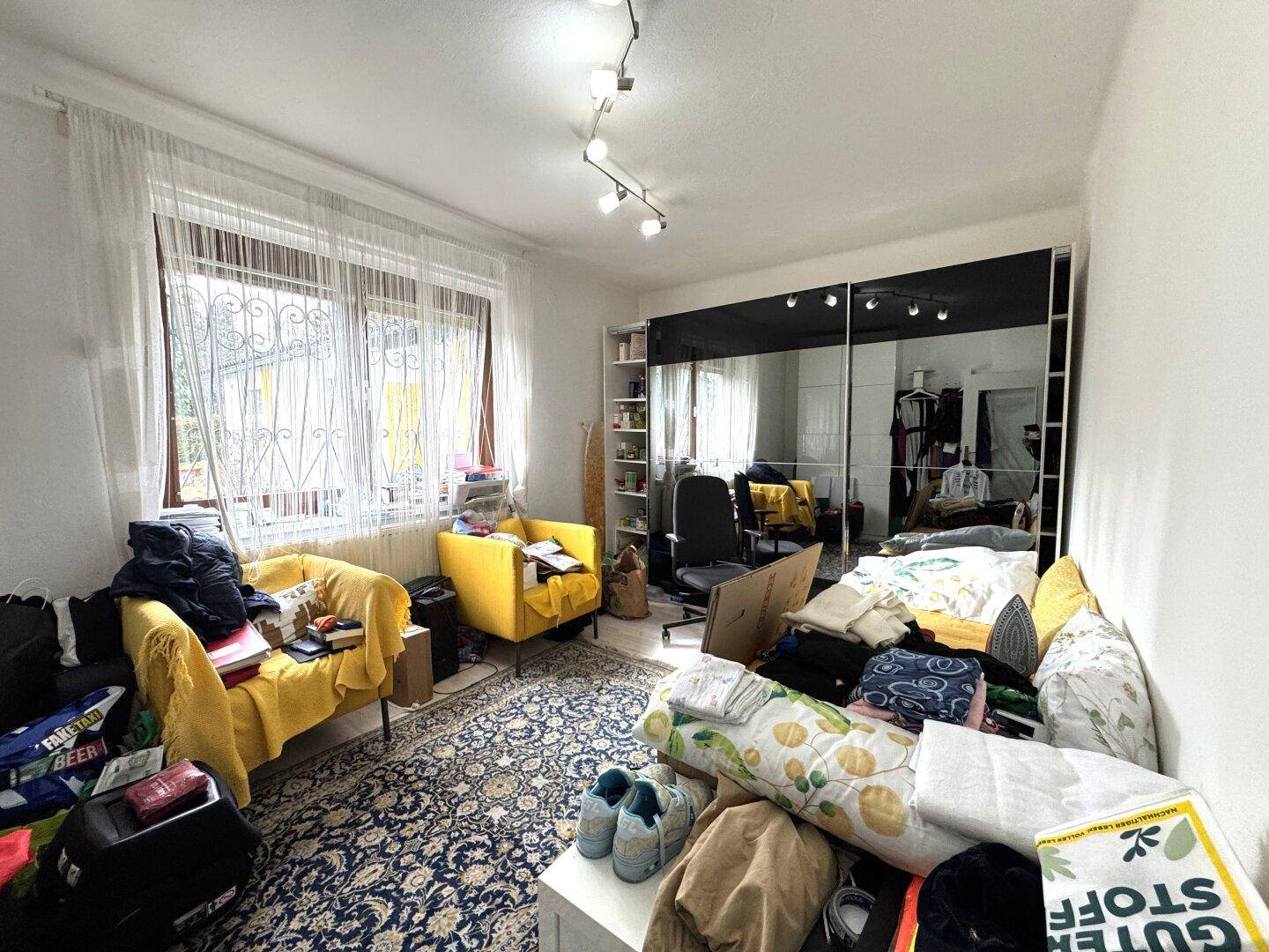 Schlafzimmer mit großem Spiegelschrank, gelben Sesseln und Fenster mit Gitter.