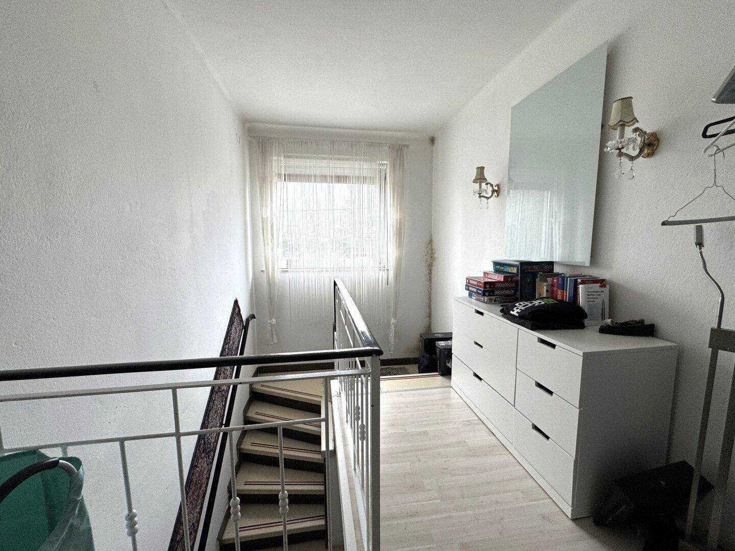 Heller Flur im Obergeschoss mit Treppenabgang, Kommode und Laminatboden.