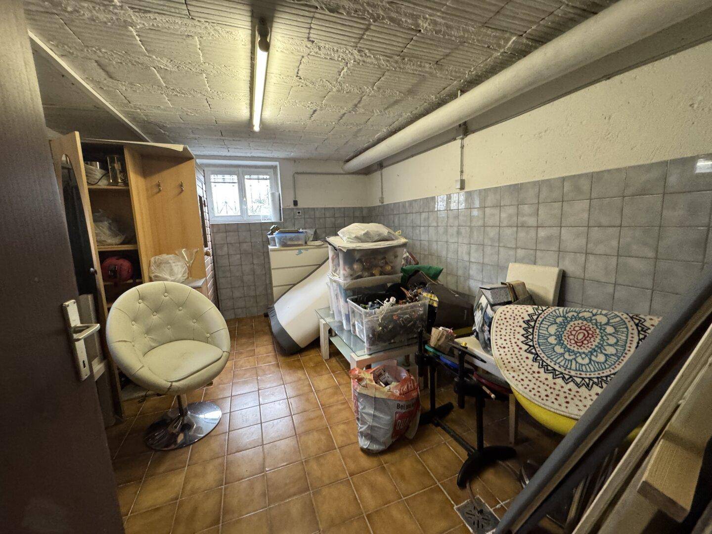Kellerraum mit Fliesenboden, Fenster und verschiedenen Lagergegenständen.