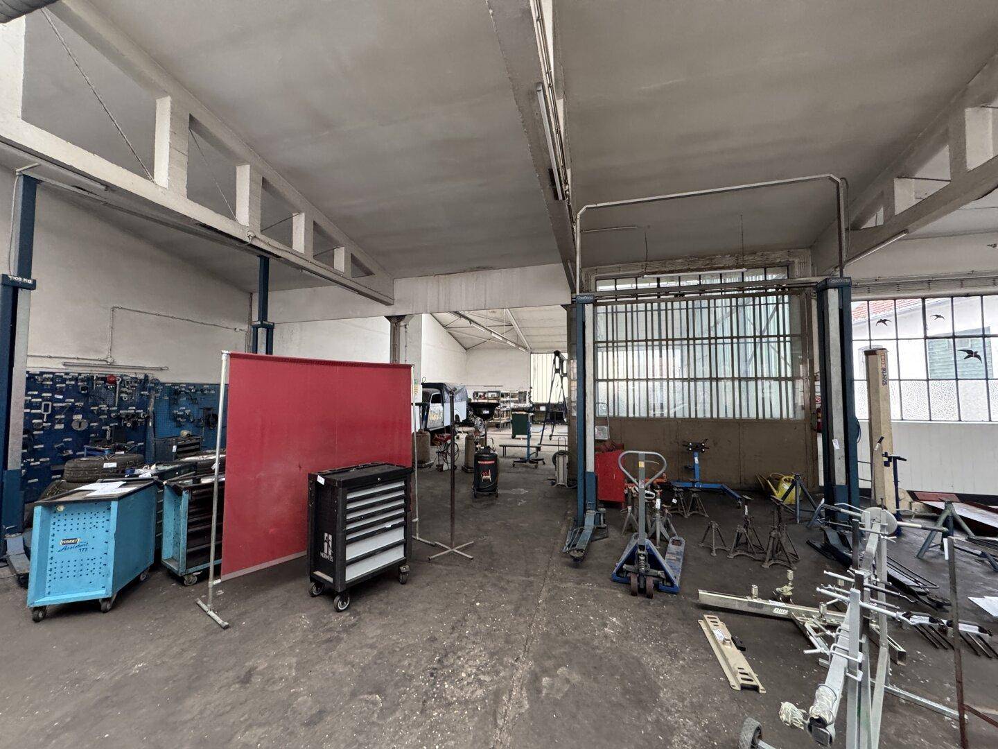 Werkstattbereich mit verschiedenen Arbeitsstationen, Werkzeugen und großen Fenstern.