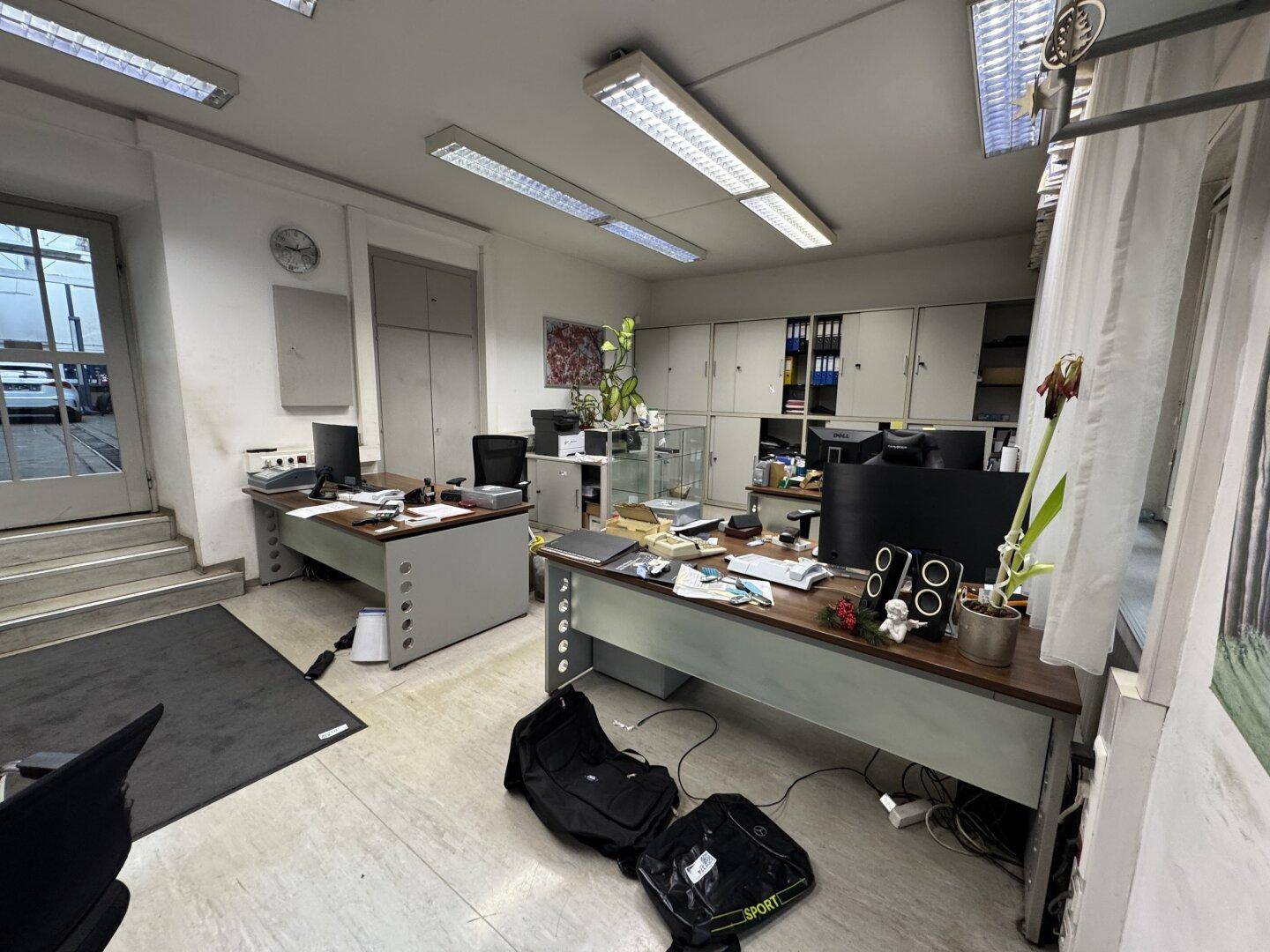 Geräumiges Büro mit mehreren Arbeitsplätzen, Aktenschränken und Fliesenboden.