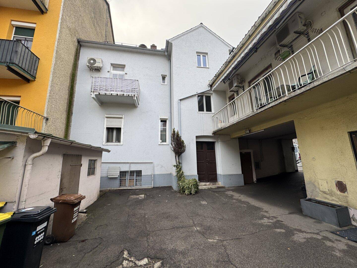 Hinterhofansicht des Gebäudes mit Zugang zum Innenhof und Mülltonnen.