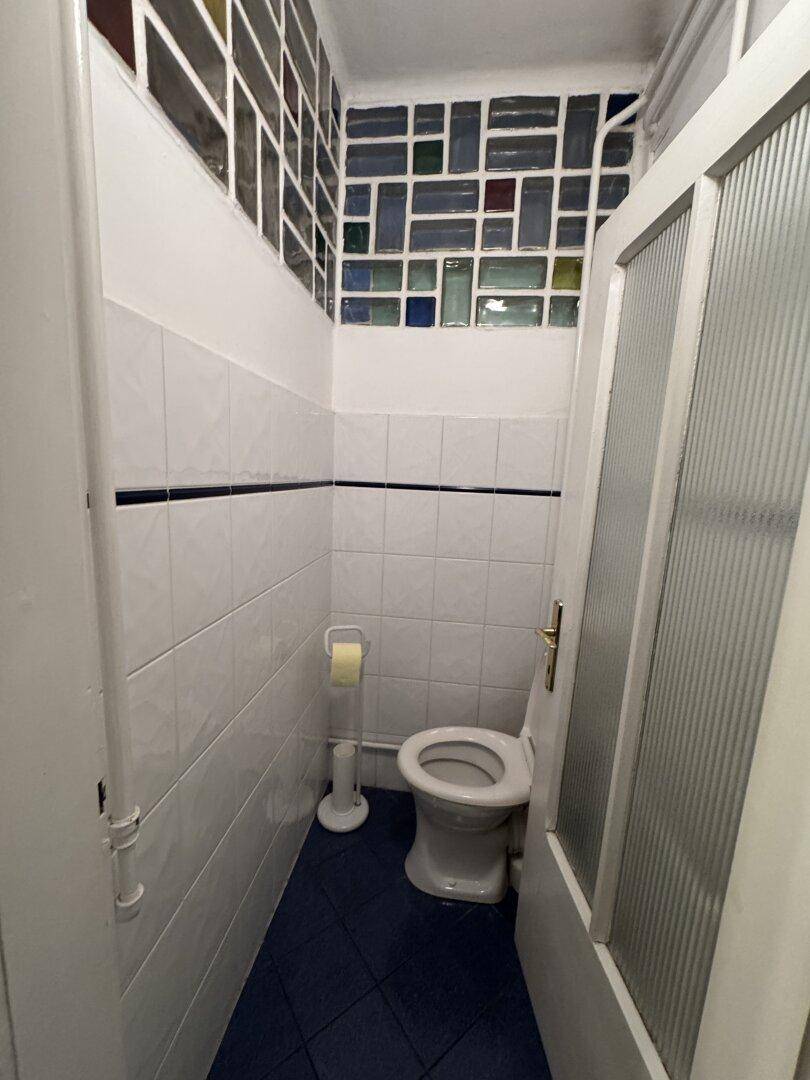 Kleines WC mit weißen Fliesen, Toilette und farbigen Glasbausteinen.