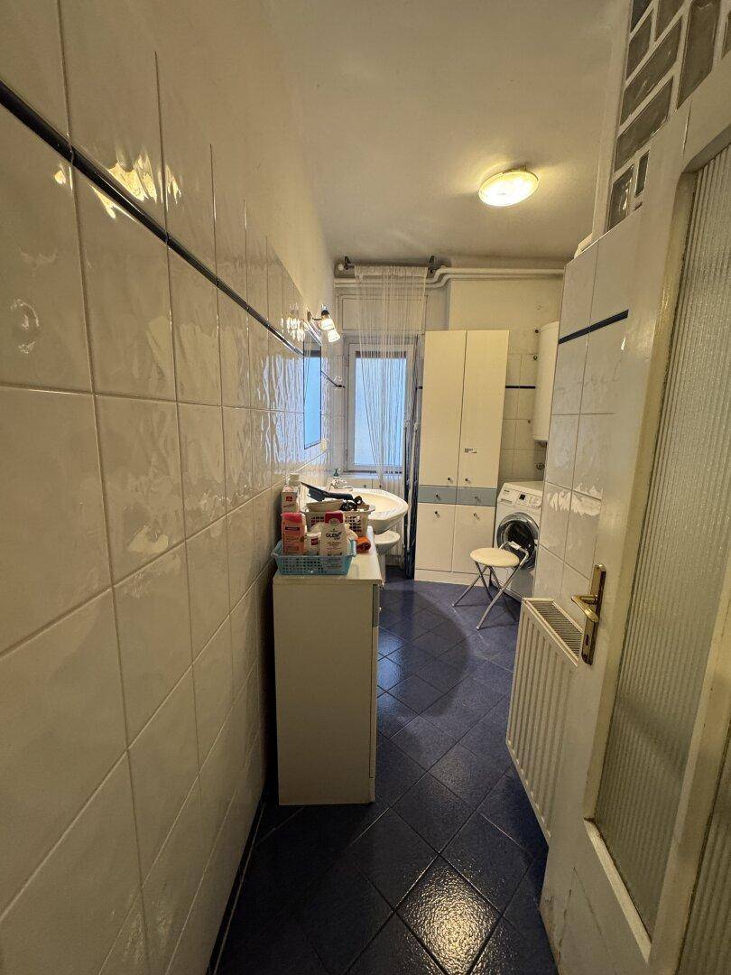 Badezimmer mit Waschbecken, Waschmaschine und weißen Fliesen an Wänden und Boden.