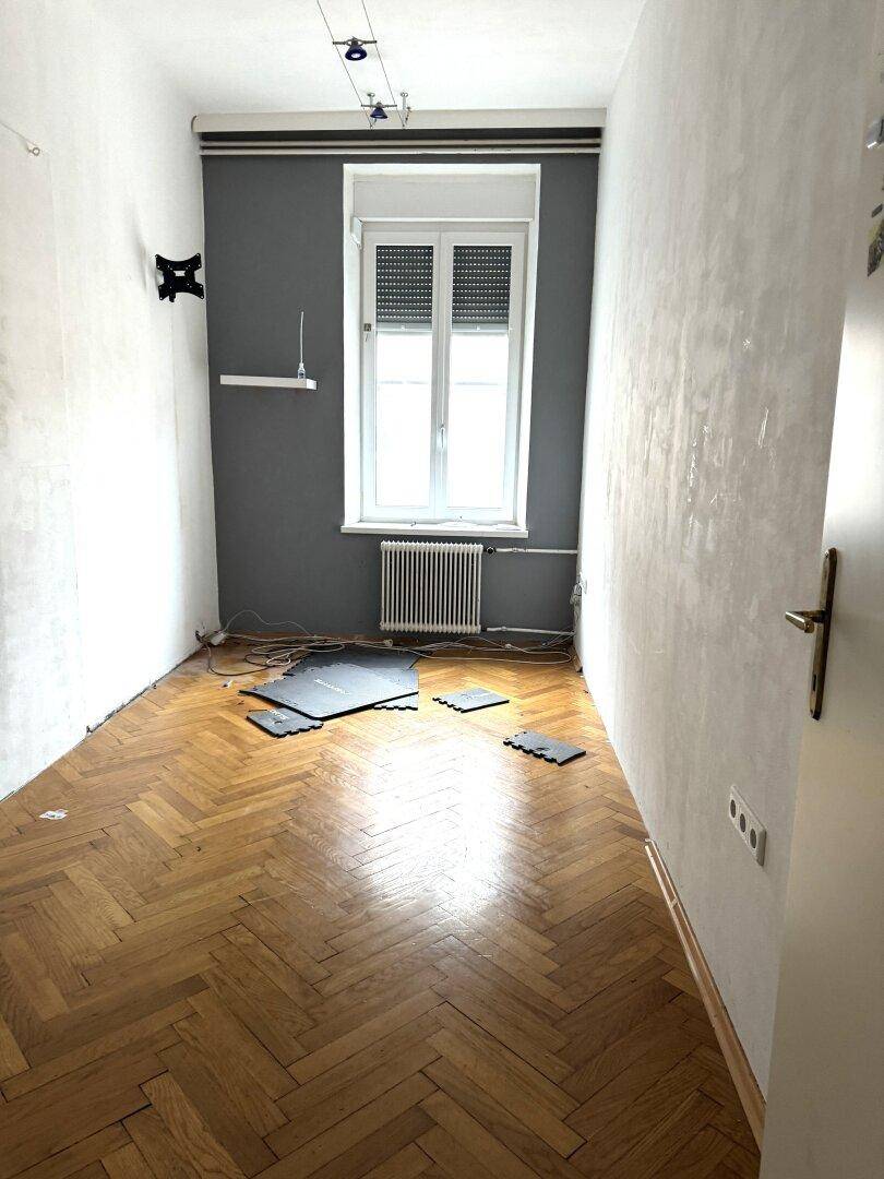 Schlafzimmer mit Fischgrätparkett, grauer Akzentwand und Fenster.