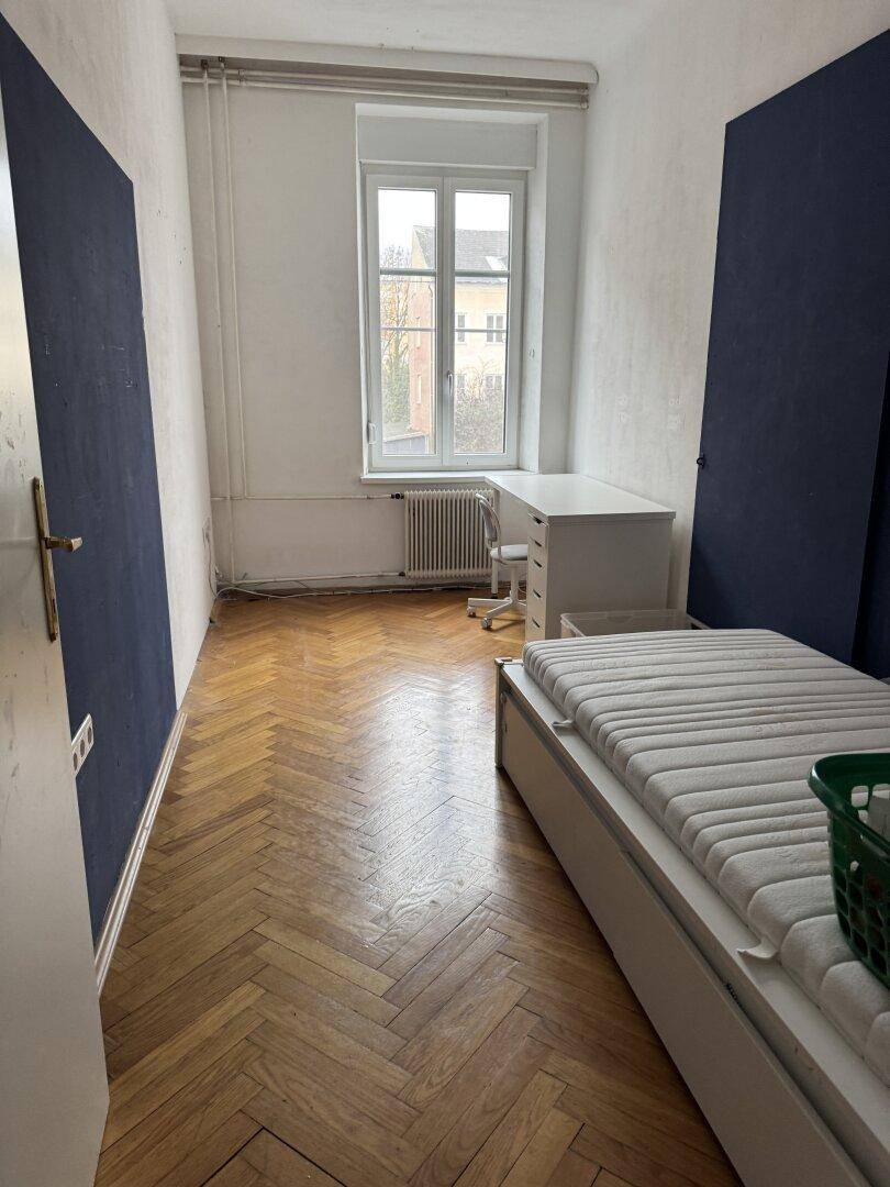 Schlafzimmer mit Parkettboden, Schreibtisch und Bett.