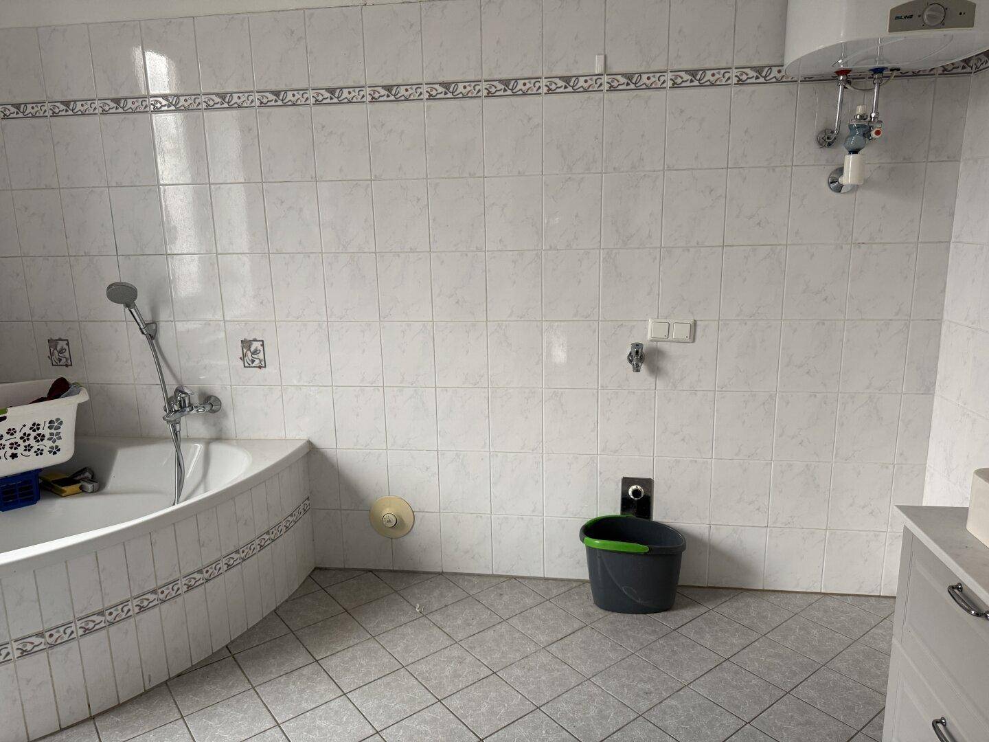 Badezimmer mit Eckbadewanne und weißen Fliesen an Wänden und Boden.