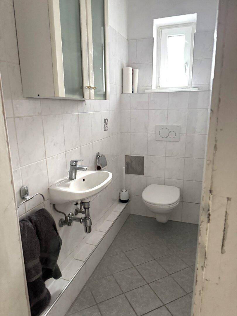Kleines WC mit Fenster, Waschbecken und weißen Fliesen.