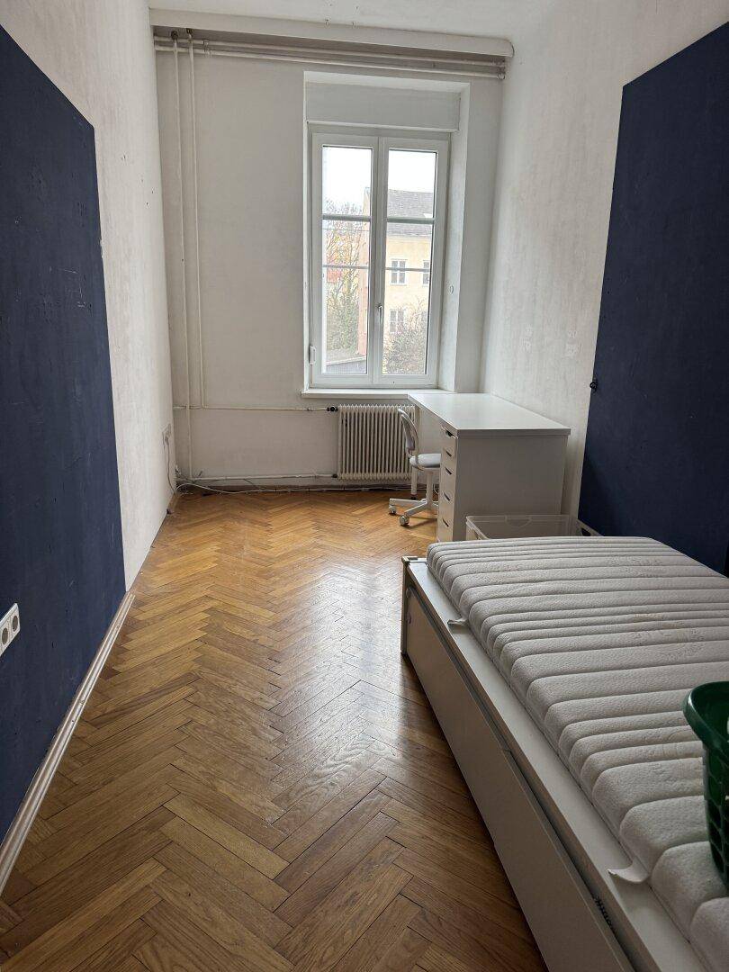 Schlafzimmer mit Parkettboden, Schreibtisch und Bett.