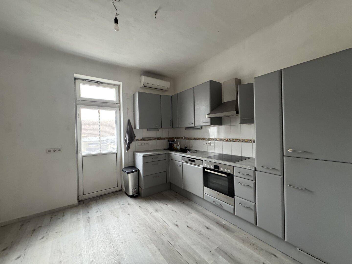 Moderne Küche mit grauen Schränken, Einbaugeräten und Laminatboden.