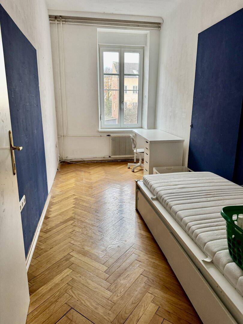 Schlafzimmer mit Parkettboden, Schreibtisch und Bett.