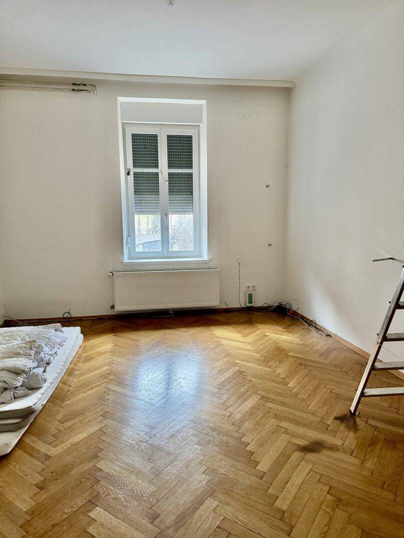 Schlafzimmer mit Fischgrätparkett und Fenster mit Rollläden.