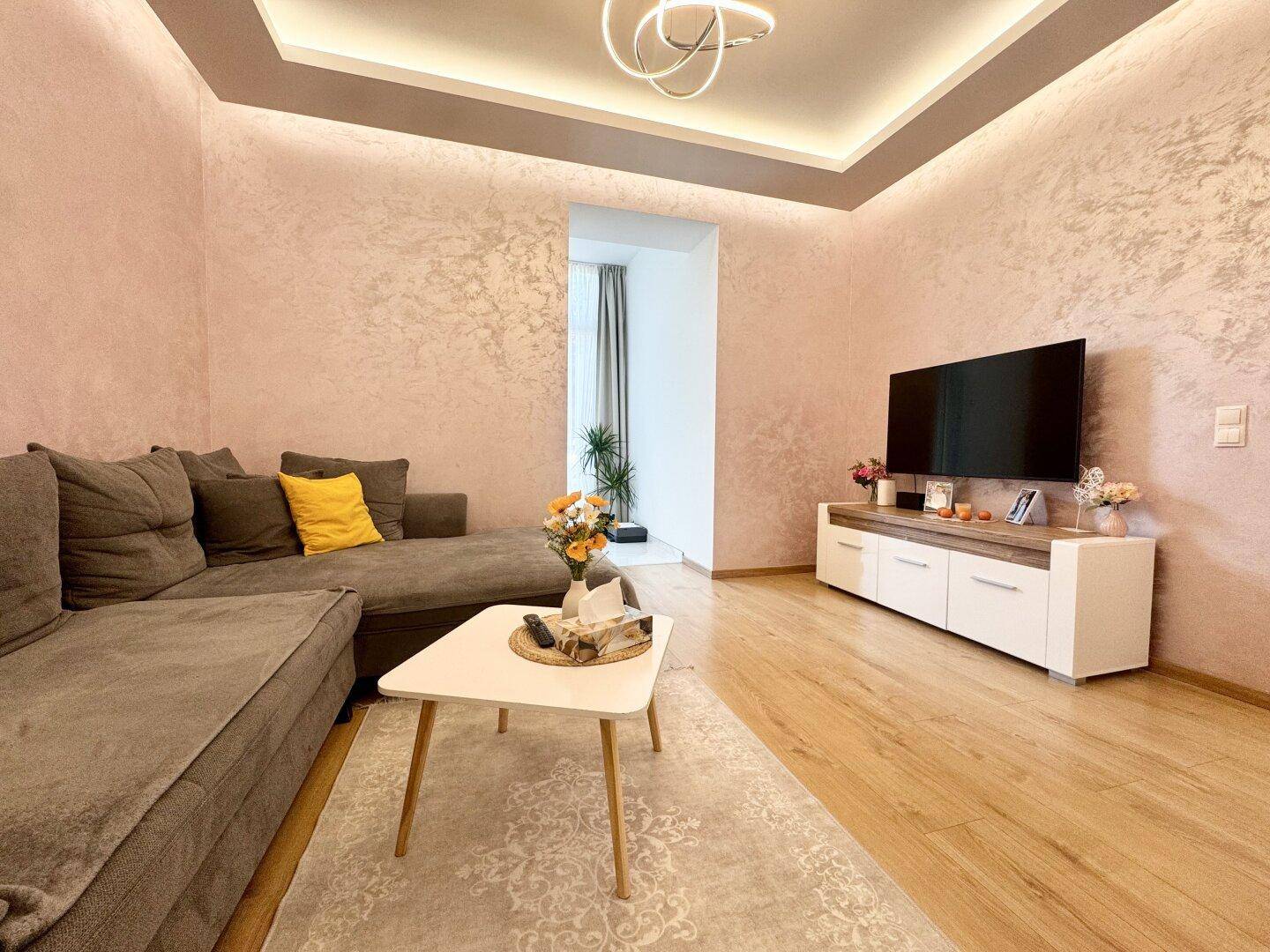 Gemütliches Wohnzimmer mit strukturierter Wandgestaltung, moderner Deckenbeleuchtung und Holzboden.
