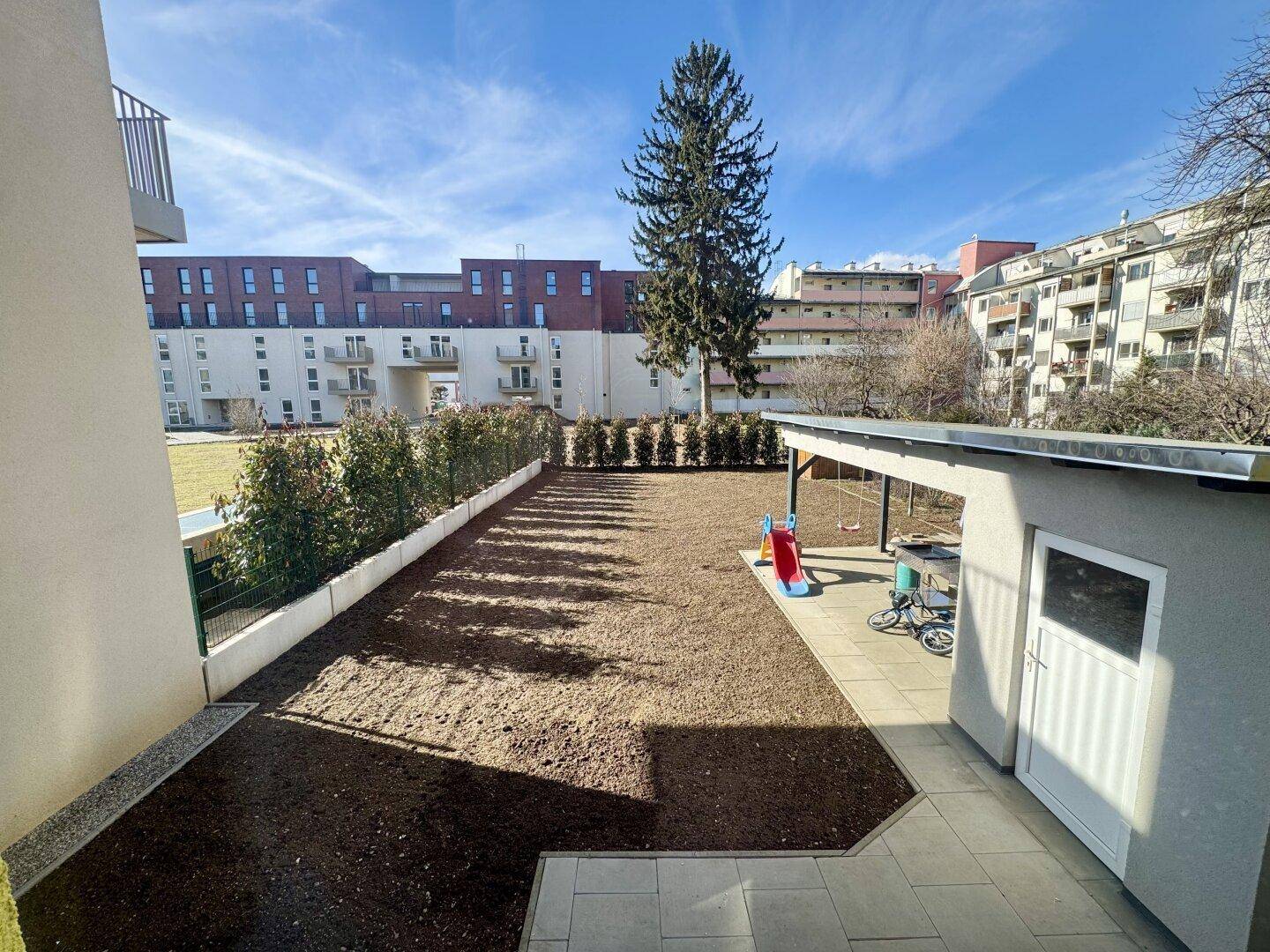 Neu angelegter Gartenbereich mit Rasenfläche, Gartenhaus, Kinderspielgeräten und Hecke.