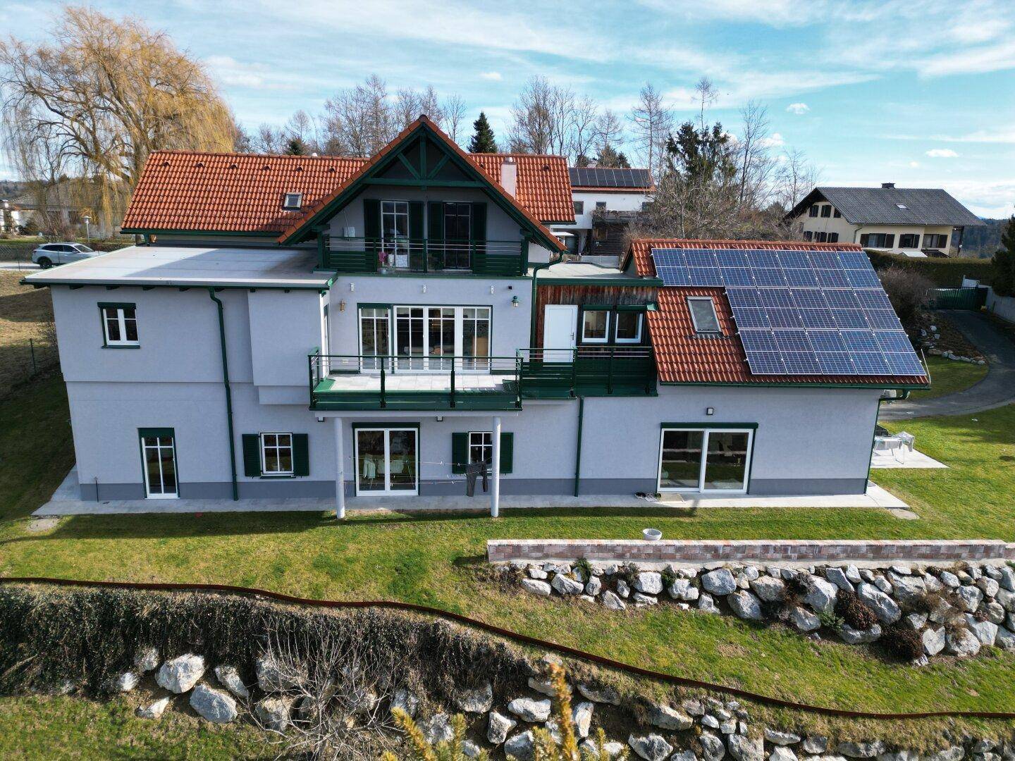 Moderne Hausfassade mit großen Fenstern, Balkonen und Solaranlage auf dem Dach unter blauem Himmel.