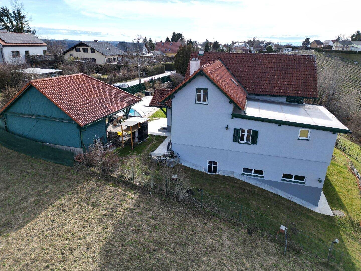 Haus in Hanglage mit angrenzendem Schuppen und Blick auf die Nachbarschaft und Landschaft.
