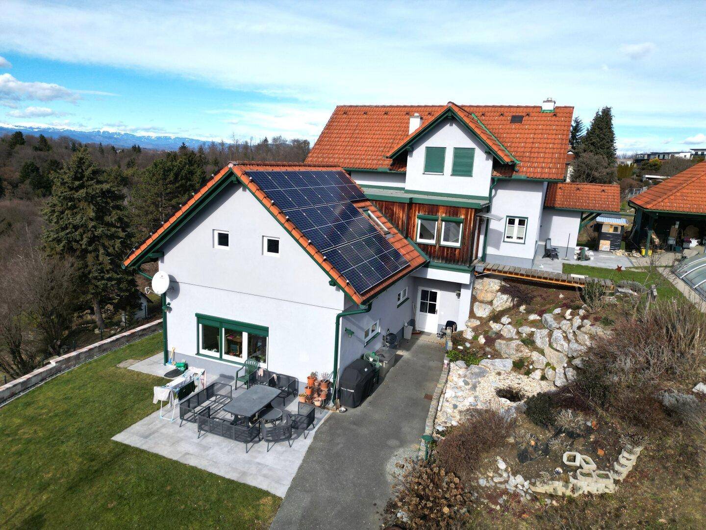 Haus mit Solaranlage, Terrasse, Gartenmöbeln und Bergblick unter blauem Himmel.