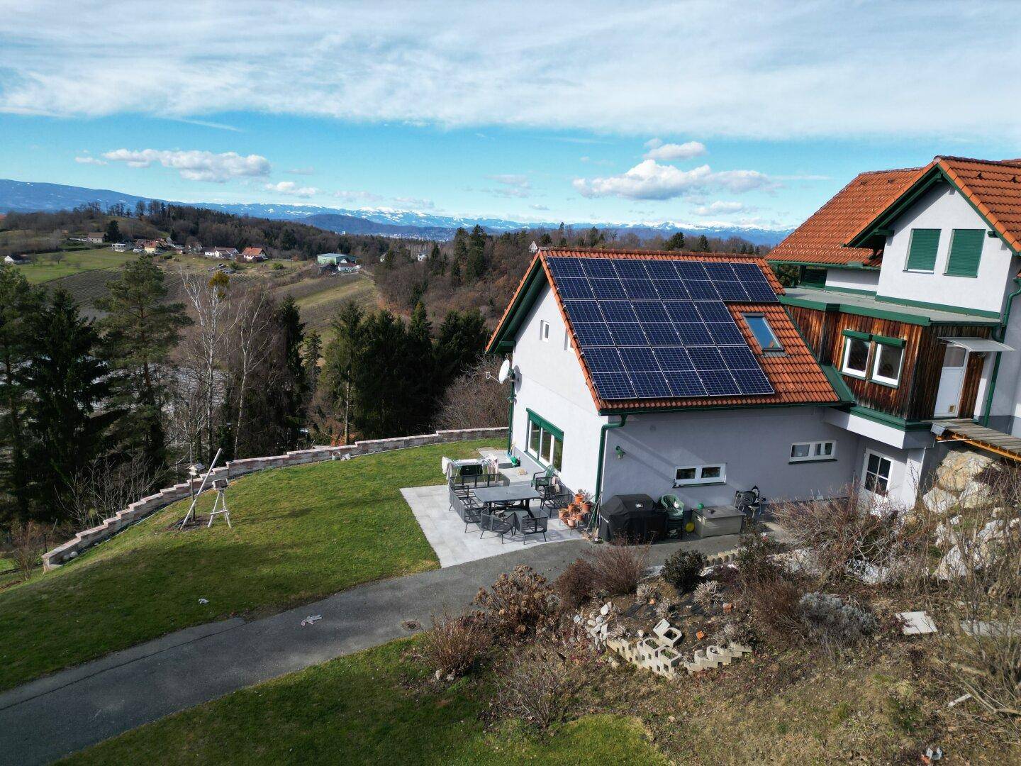 Luftaufnahme eines Hauses mit Photovoltaikanlage, Terrasse und weitläufigem Gartenbereich.