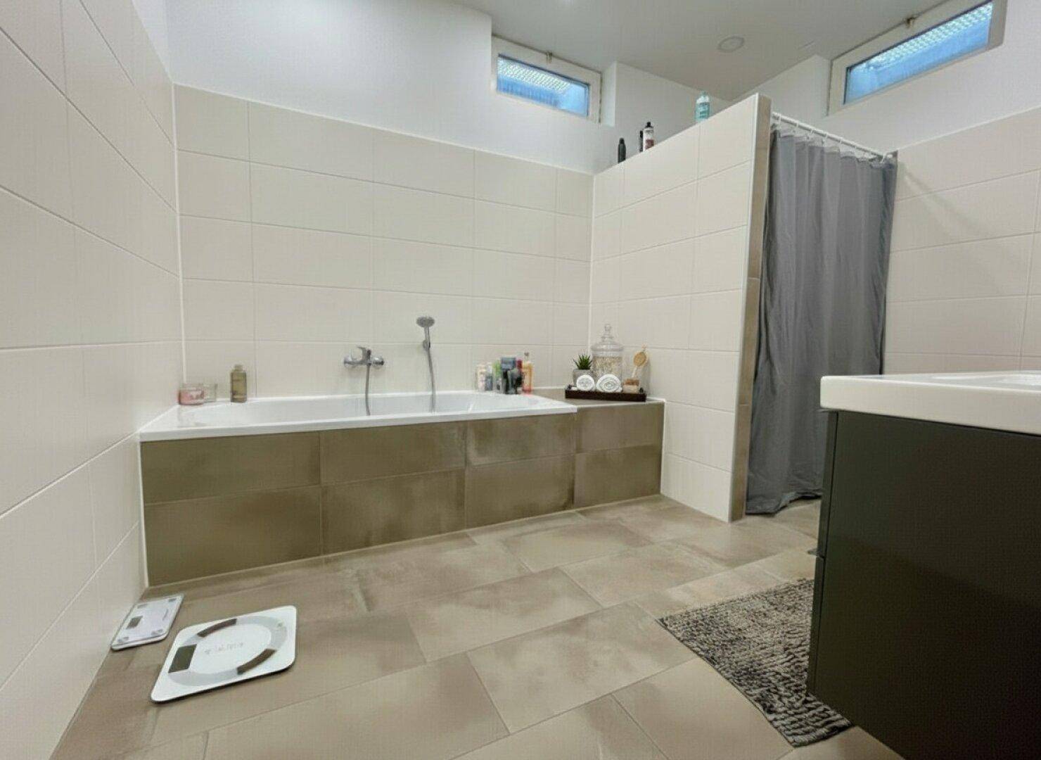 Modernes Badezimmer mit Badewanne, Duschbereich und hellen Fliesen.