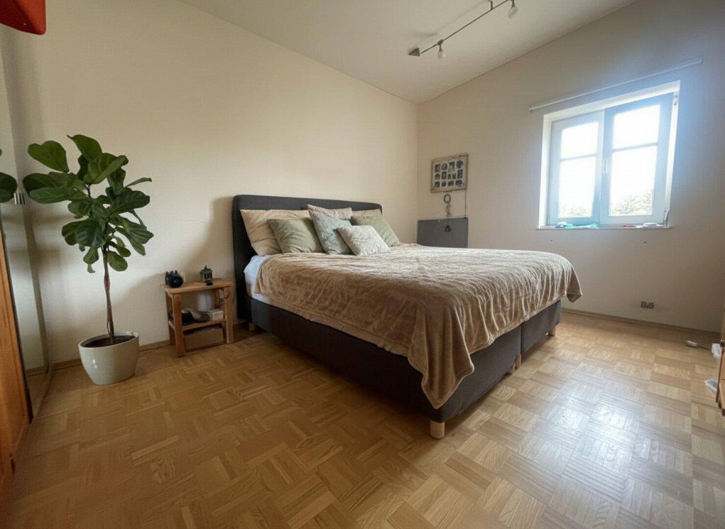 Helles Schlafzimmer mit Parkettboden, großem Bett und Fenster für viel Tageslicht.