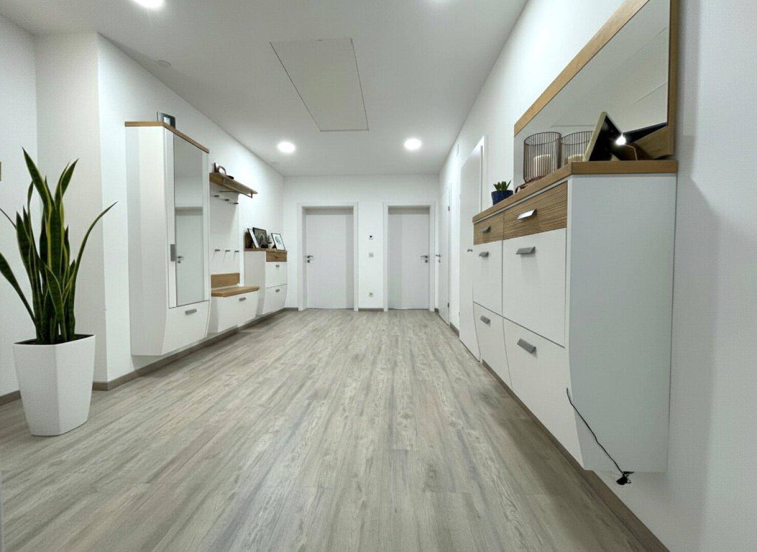 Heller Flur mit modernem Garderobenschrank, Spiegel und Holzoptik-Boden.