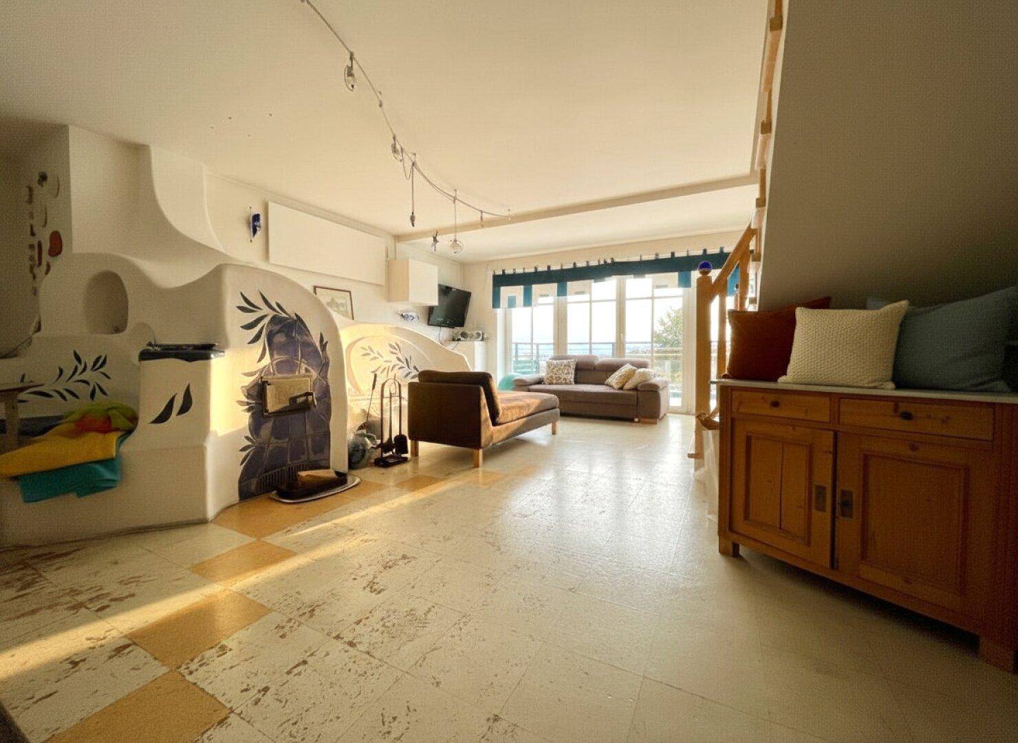 Geräumiges Wohnzimmer mit Kachelofen, Sitzbereich und Zugang zu einem Balkon.