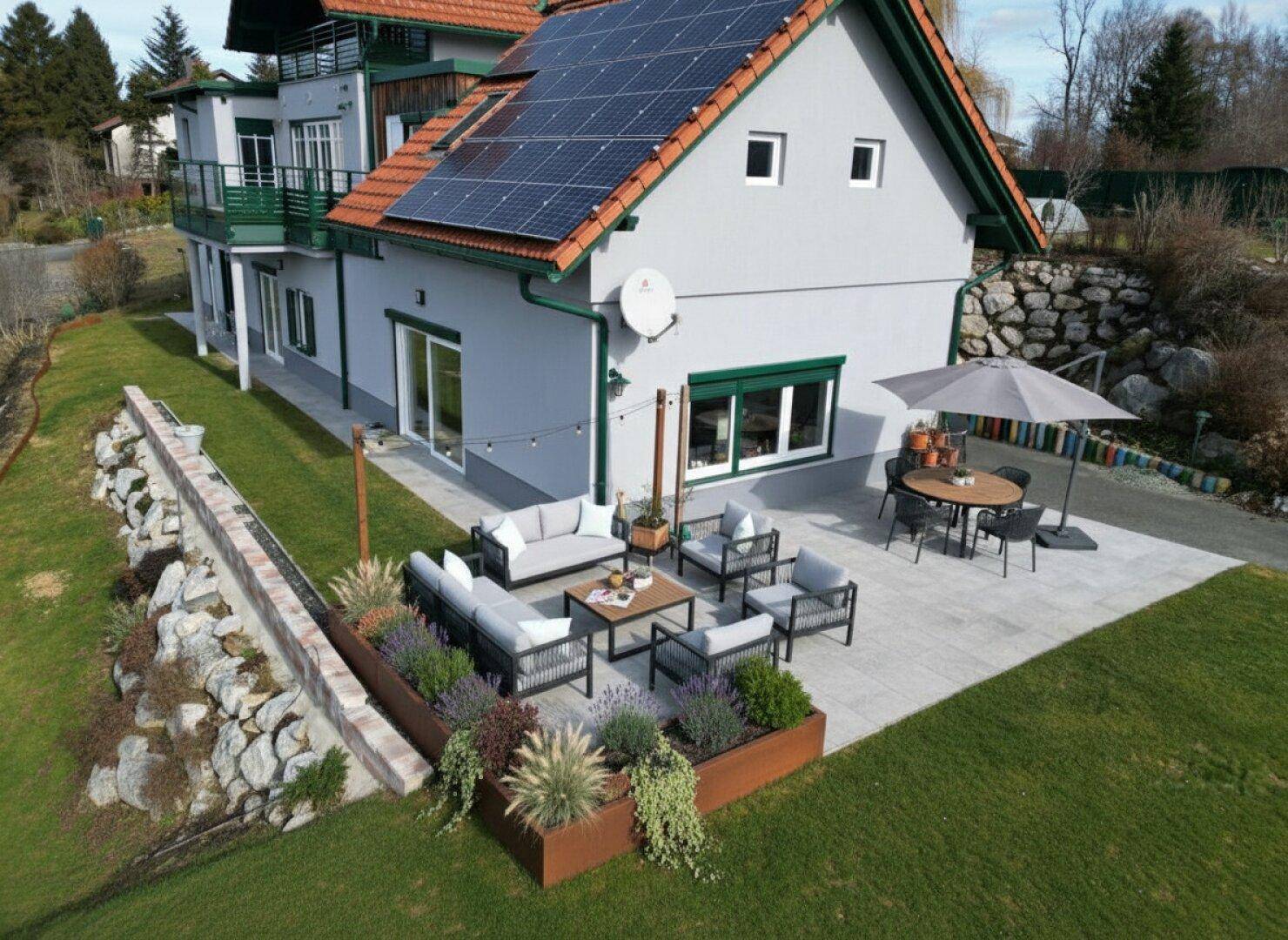 Große gepflasterte Terrasse mit modernen Gartenmöbeln, Essbereich und bepflanzten Hochbeeten.