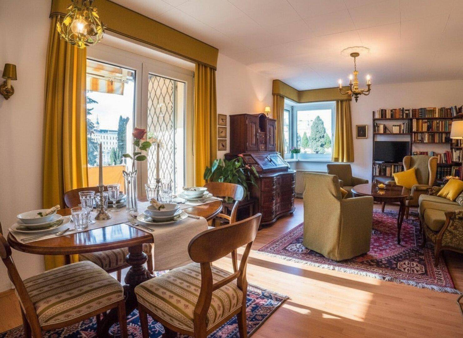 Klassisch eingerichteter Wohn-Essbereich mit Holzboden, Teppich und Zugang zum Balkon.