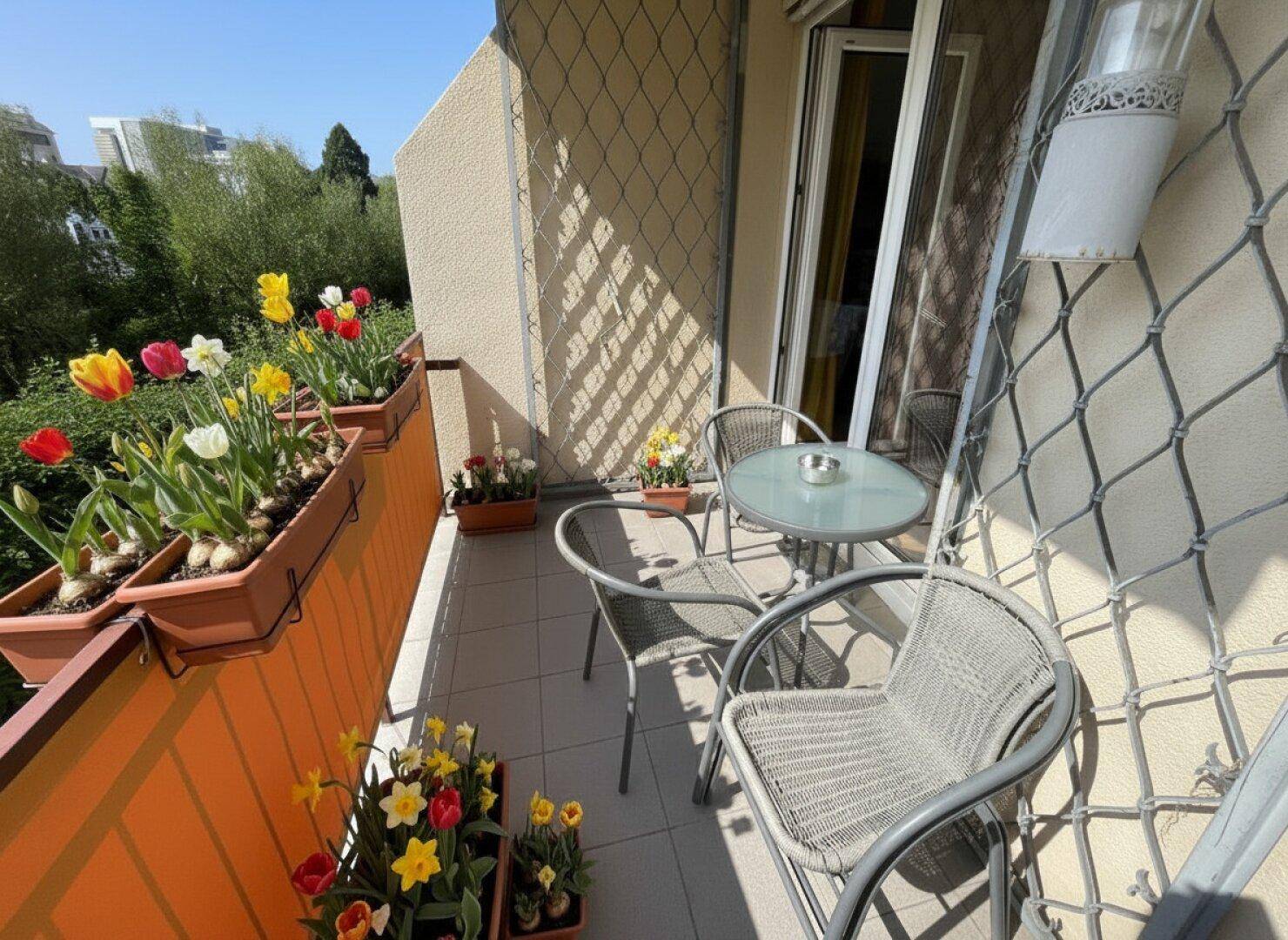 Sonniger Balkon mit Metallmöbeln und bunten Blumenkästen, ideal zum Entspannen.