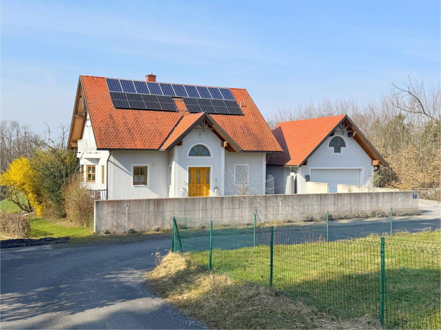 Das Einfamilienhaus von der Straße aus gesehen, mit Photovoltaikanlage und umgebender Naturlandschaft.
