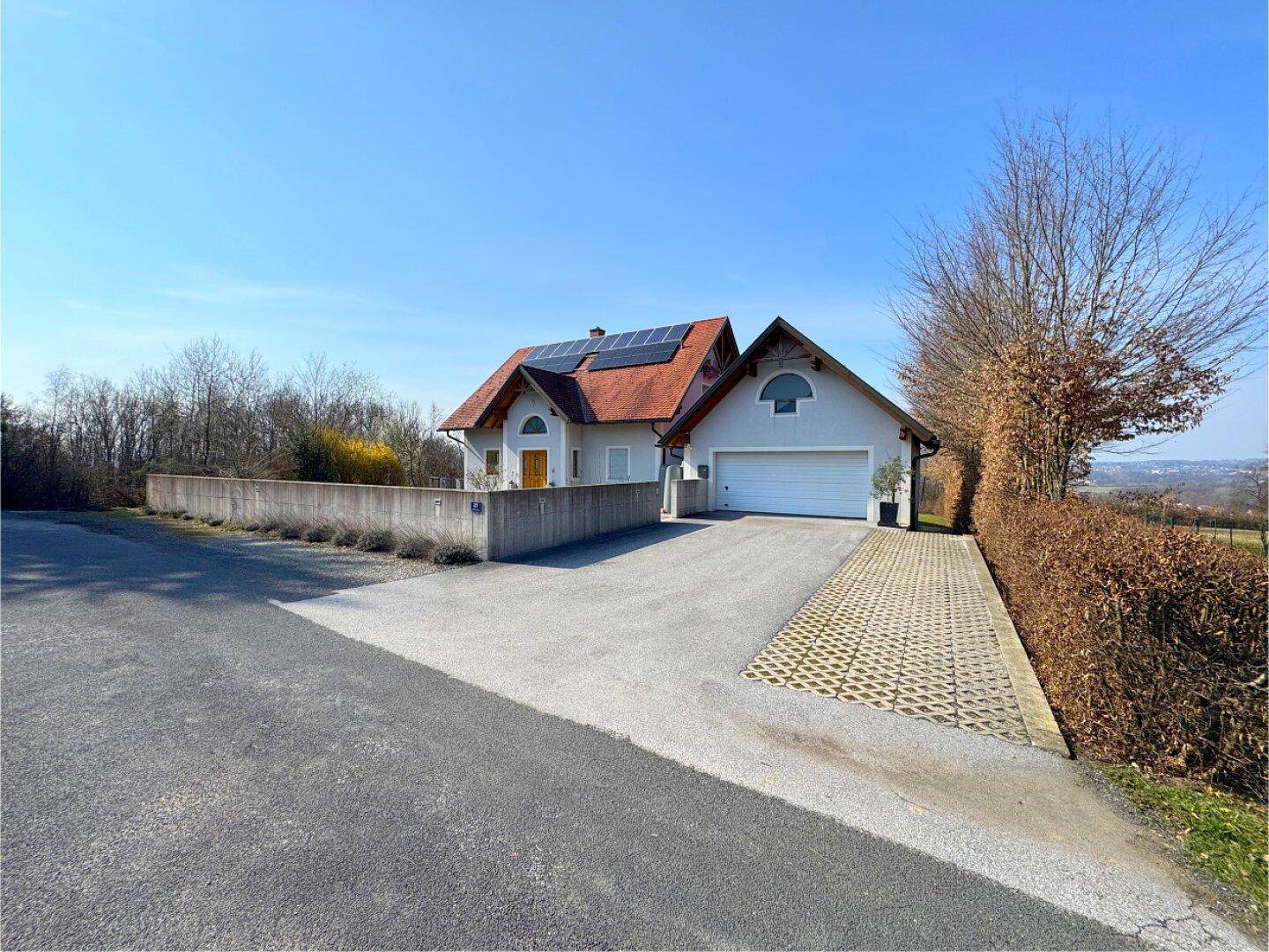 Weitläufige Zufahrt zum Haus mit integrierter Garage und Photovoltaikanlage auf dem Dach unter blauem Himmel.
