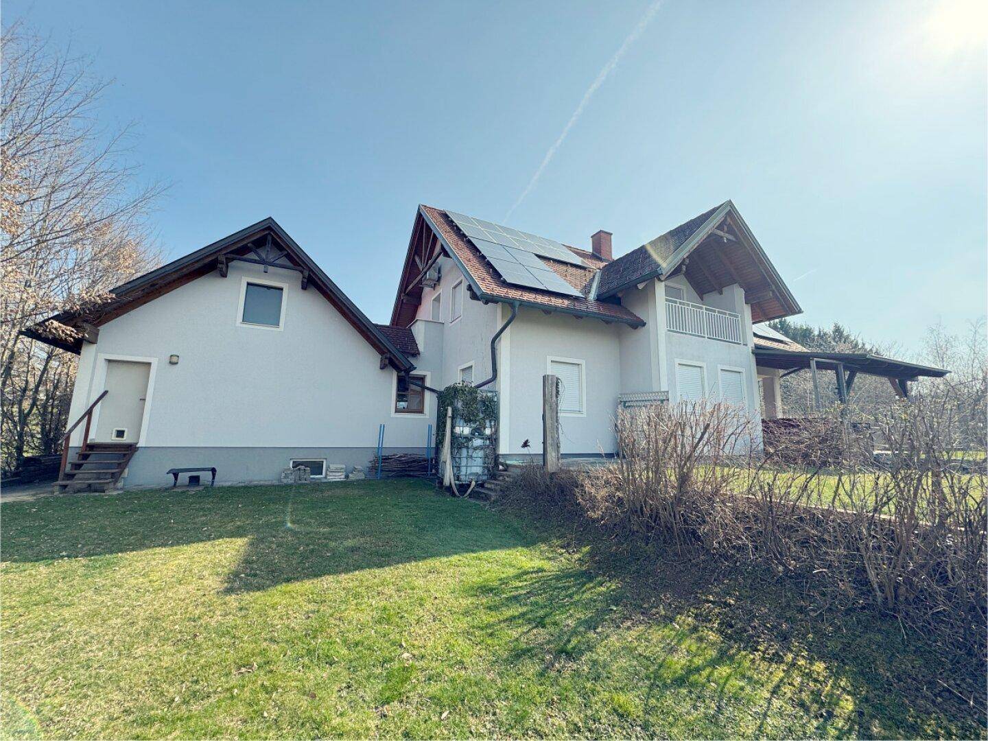 Seitenansicht des Hauses mit Garage und weitläufigem Gartenbereich unter blauem Himmel.