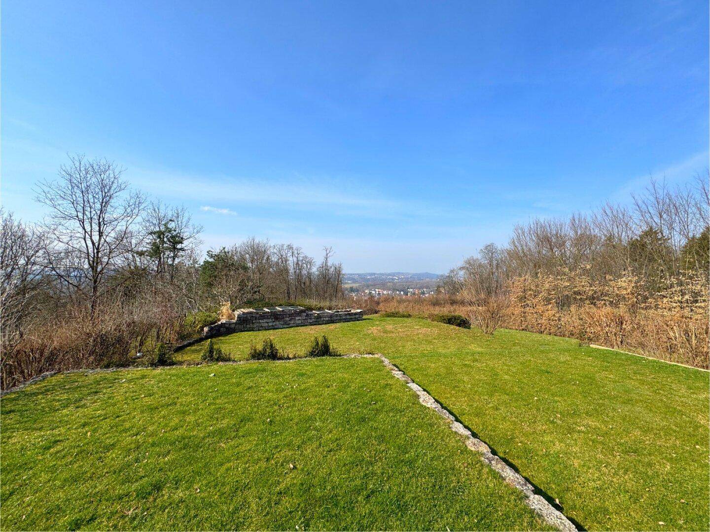 Sonniger Garten mit weitem Blick über die grüne Landschaft und die Ferne.