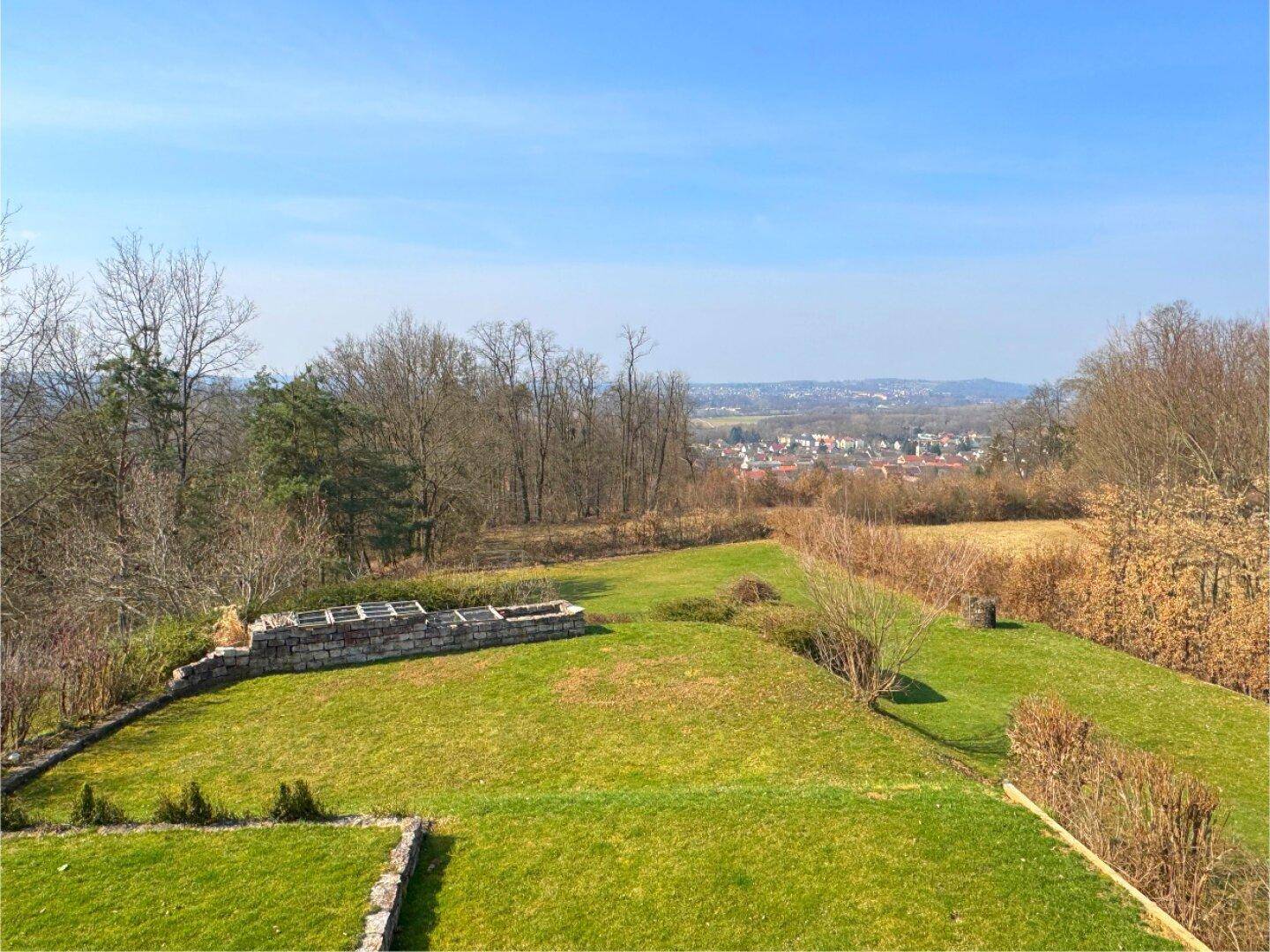 Panoramablick vom oberen Balkon auf den gepflegten Garten und die weite Landschaft.