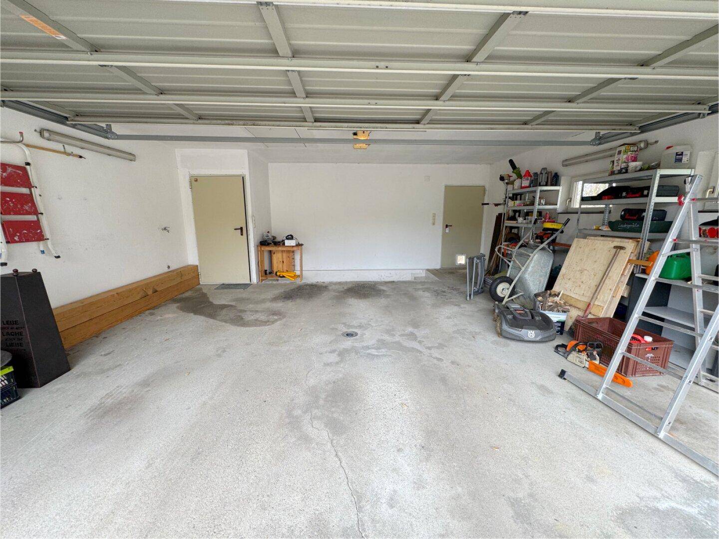 Geräumige Garage mit Betonboden, Stauraum und verschiedenen Werkzeugen.