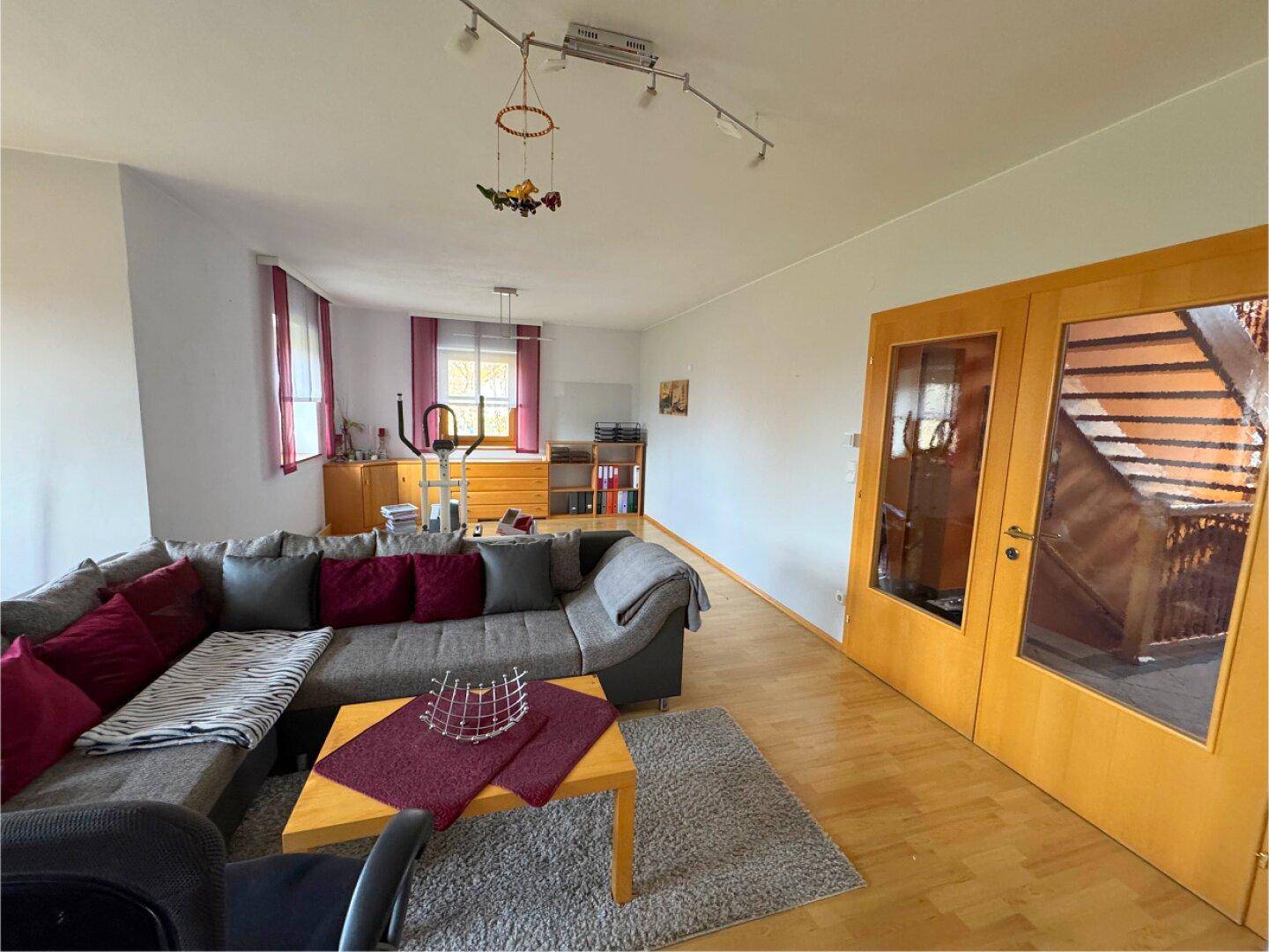 Gemütliches Wohnzimmer mit großem Ecksofa, Holzboden und Zugang zu weiteren Räumen.