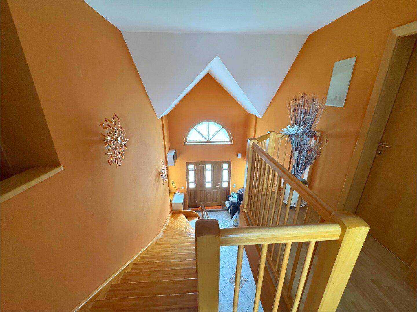 Blick von der Treppe auf den Eingangsbereich mit Holztür und Rundbogenfenster.