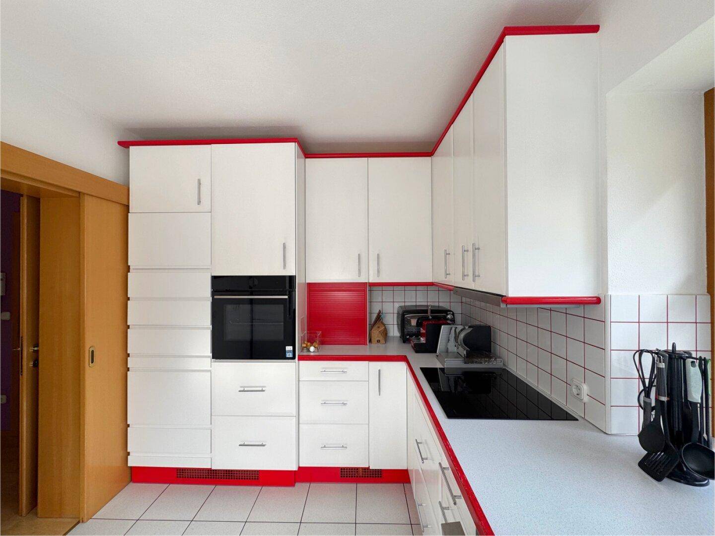 Moderne Einbauküche mit integriertem Backofen, weißen Schränken und roten Details.