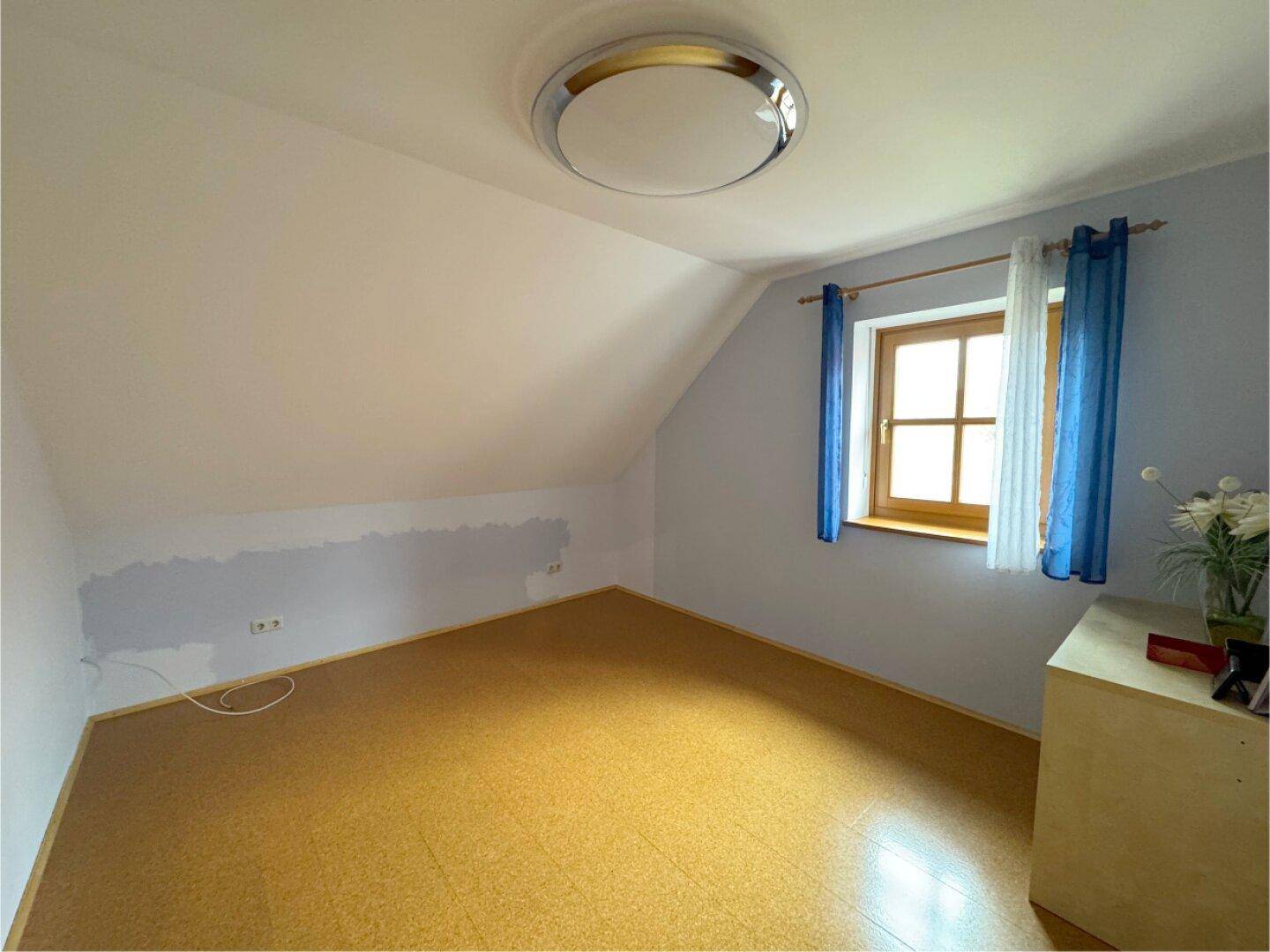 Helles Schlafzimmer mit Dachschräge, Fenster und Korkboden.