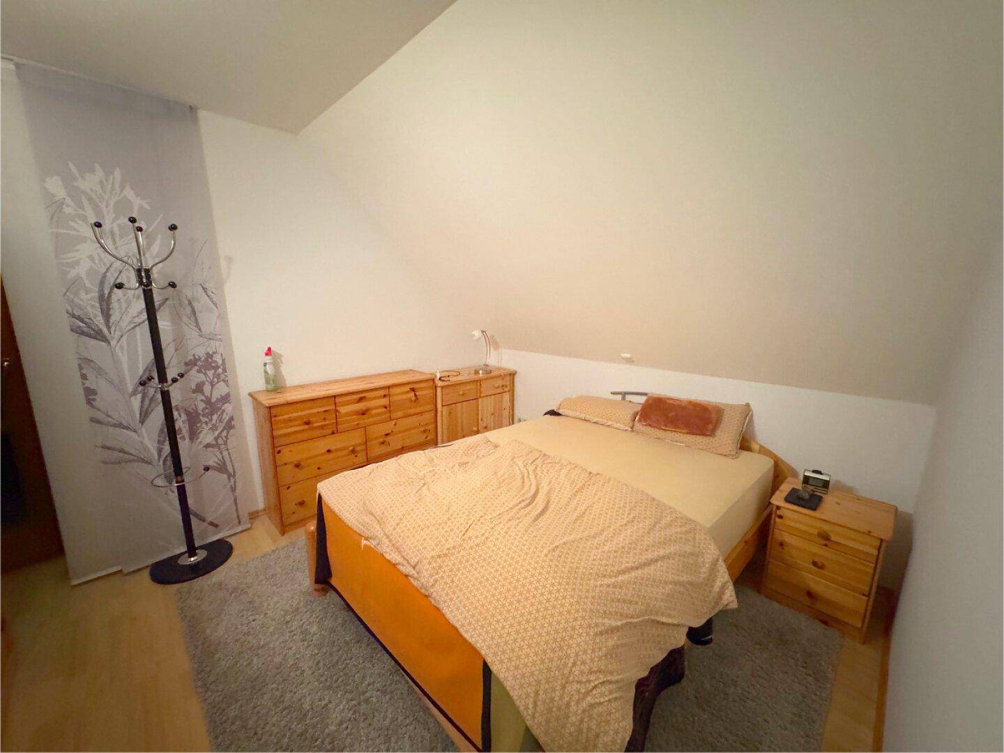 Gemütliches Schlafzimmer mit Holzbett, Kommoden und Teppichboden unter der Dachschräge.