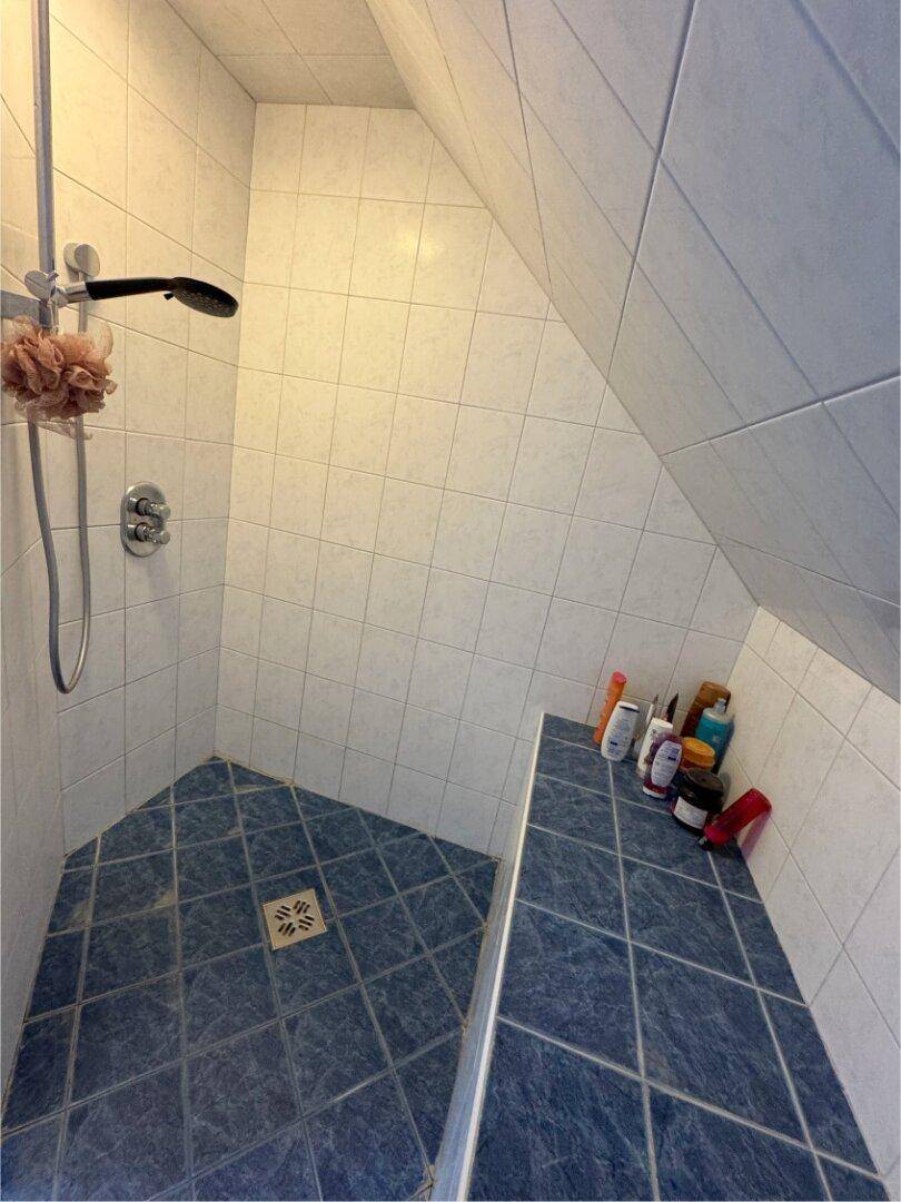 Duschbereich im Badezimmer mit blauen und weißen Fliesen und Dachschräge.