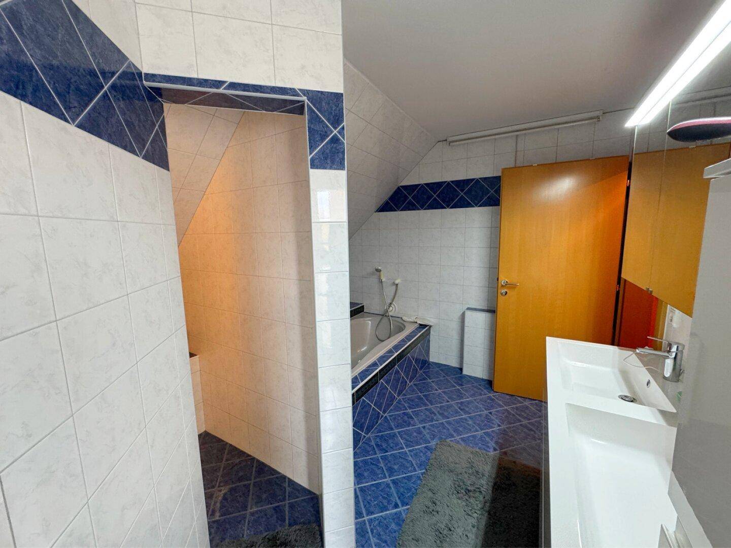 Badezimmer mit Waschbecken, Spiegel und Zugang zu weiteren Räumen.